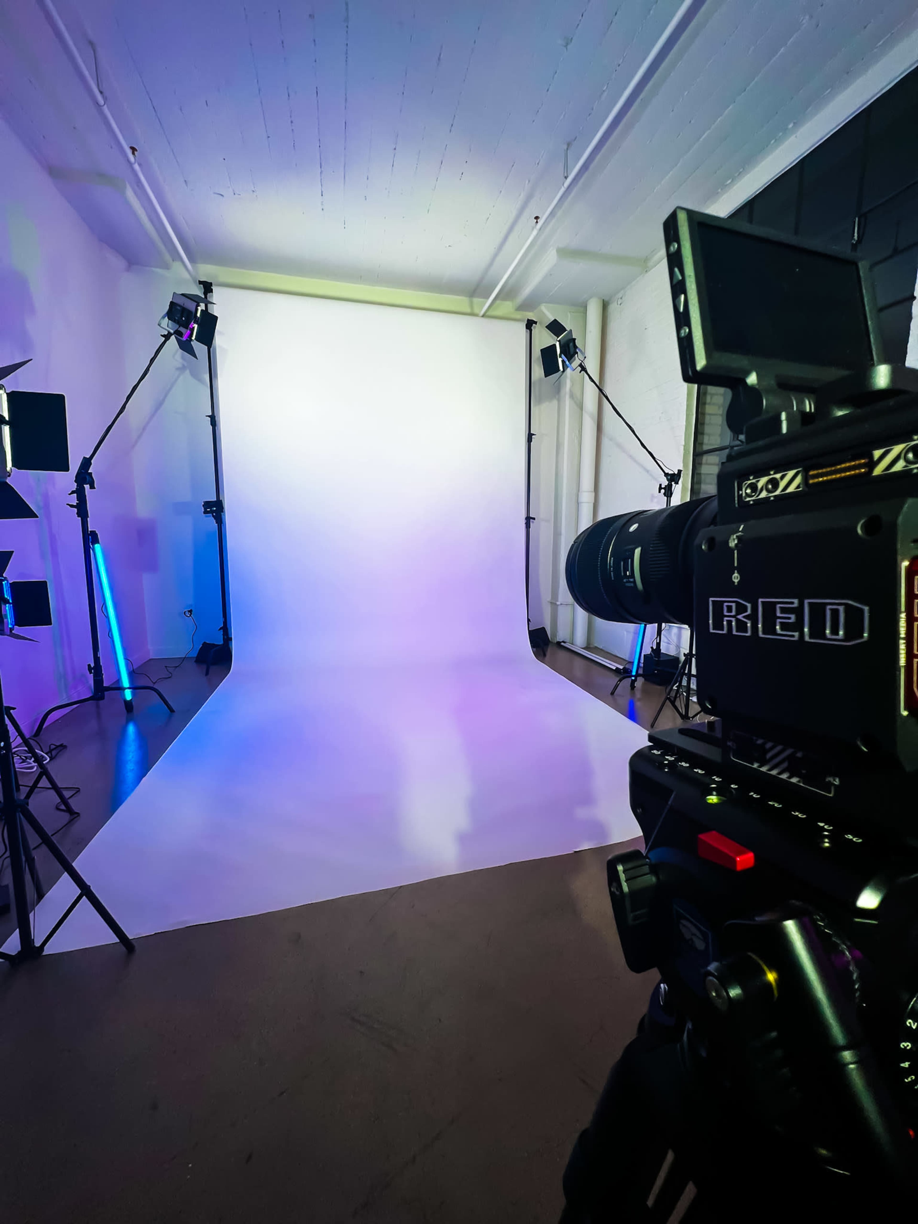 A professional photography studio features a white backdrop with lighting equipment and a RED camera positioned in the foreground.