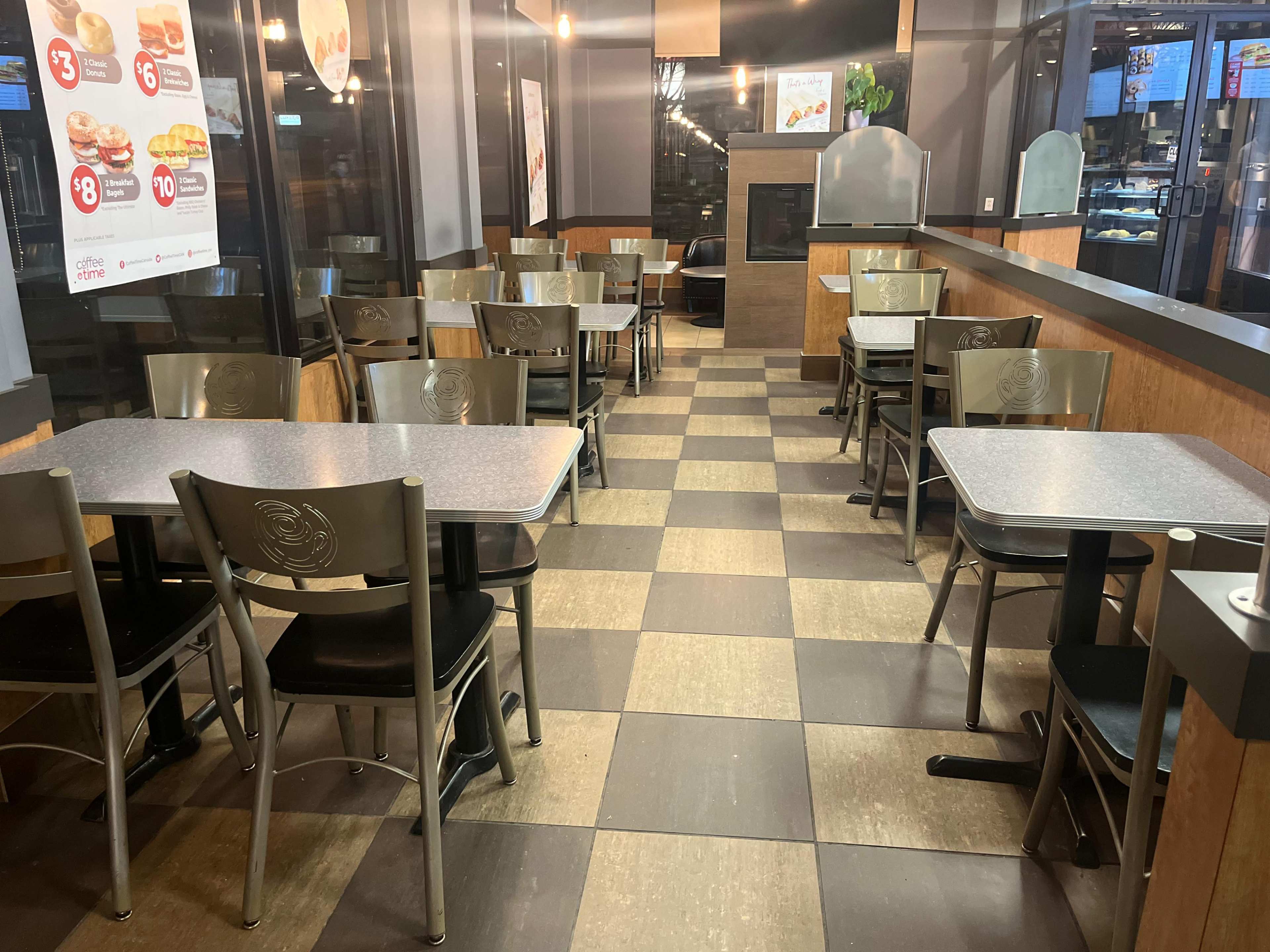 The image shows an empty fast-food restaurant with metal tables and chairs arranged in a checkered floor layout.