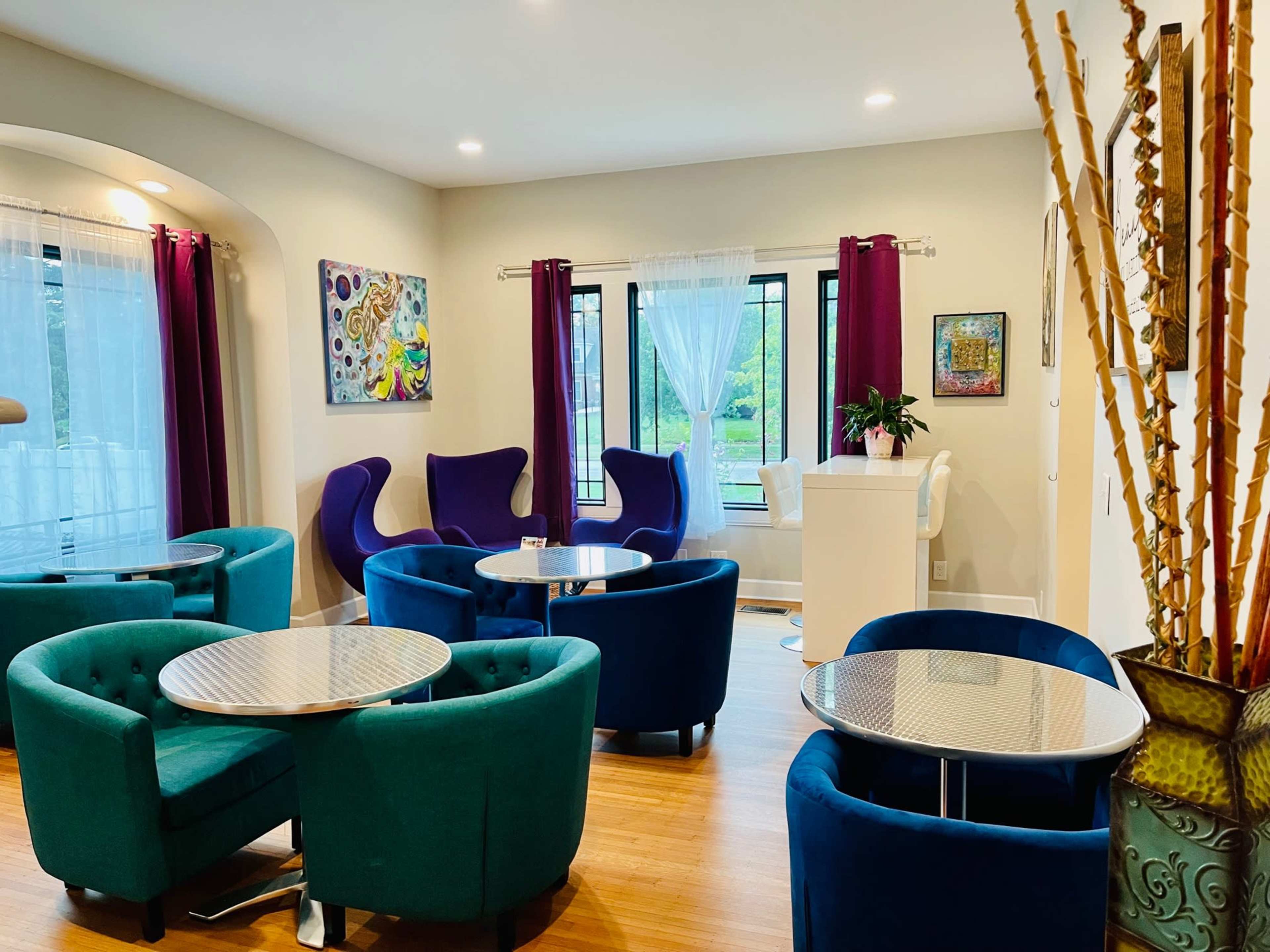 The image shows a stylish, modern lounge area with colorful seating and tables arranged around a bright, spacious interior.