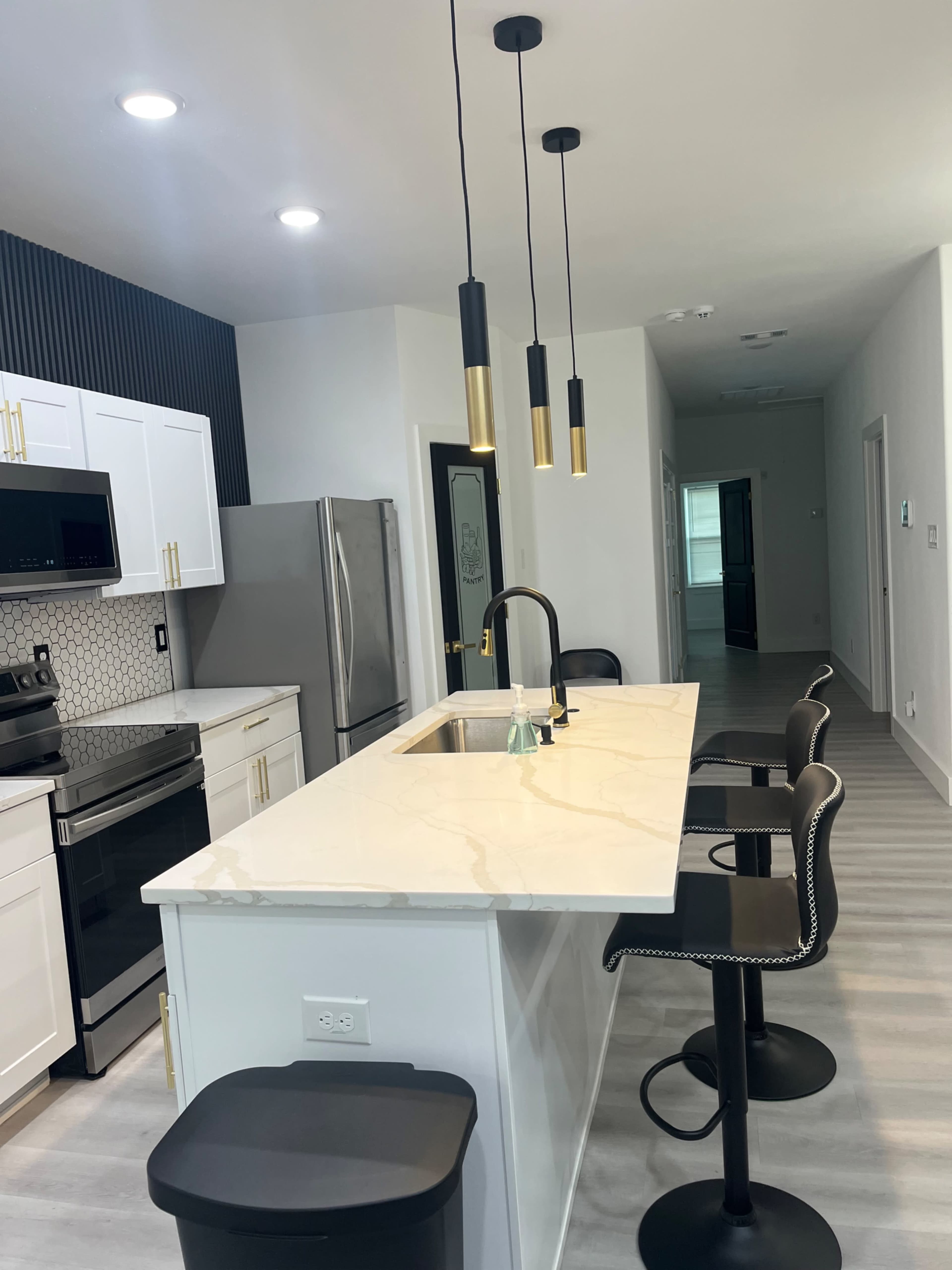 The image shows a modern kitchen with white cabinetry, a large marble island with black bar stools, and sleek pendant lighting.