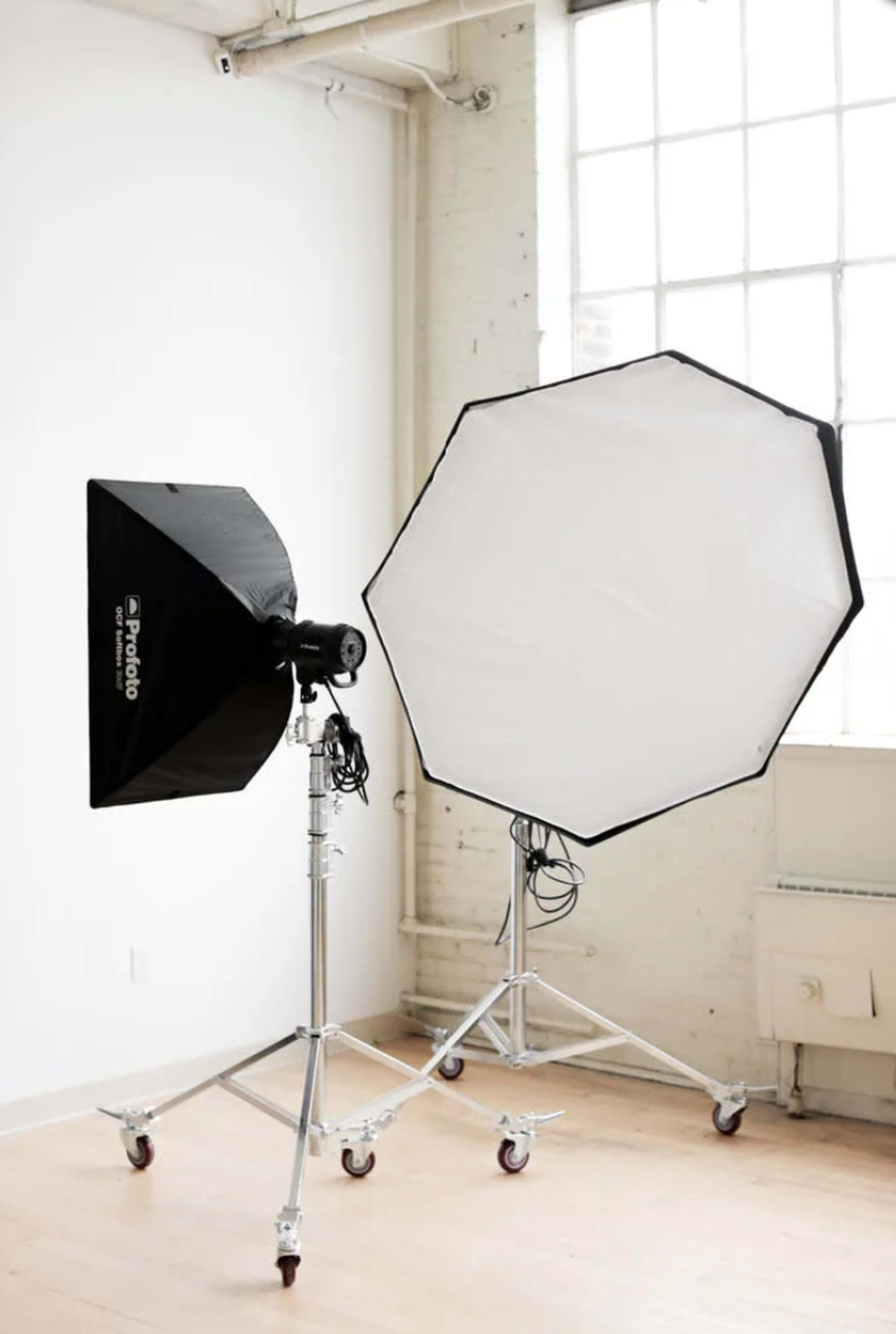 Two studio lighting setups, including a rectangular softbox and an octagonal softbox, positioned in a brightly lit room with large windows.