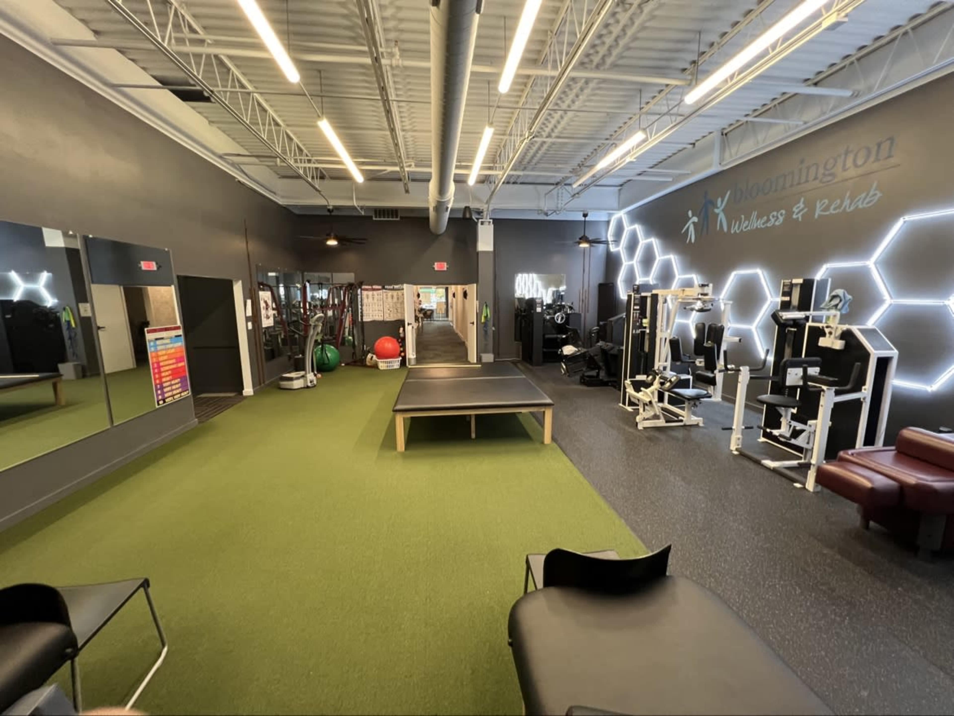 The image shows a fitness and wellness center with exercise equipment, a green turf area, and a mirrored wall.