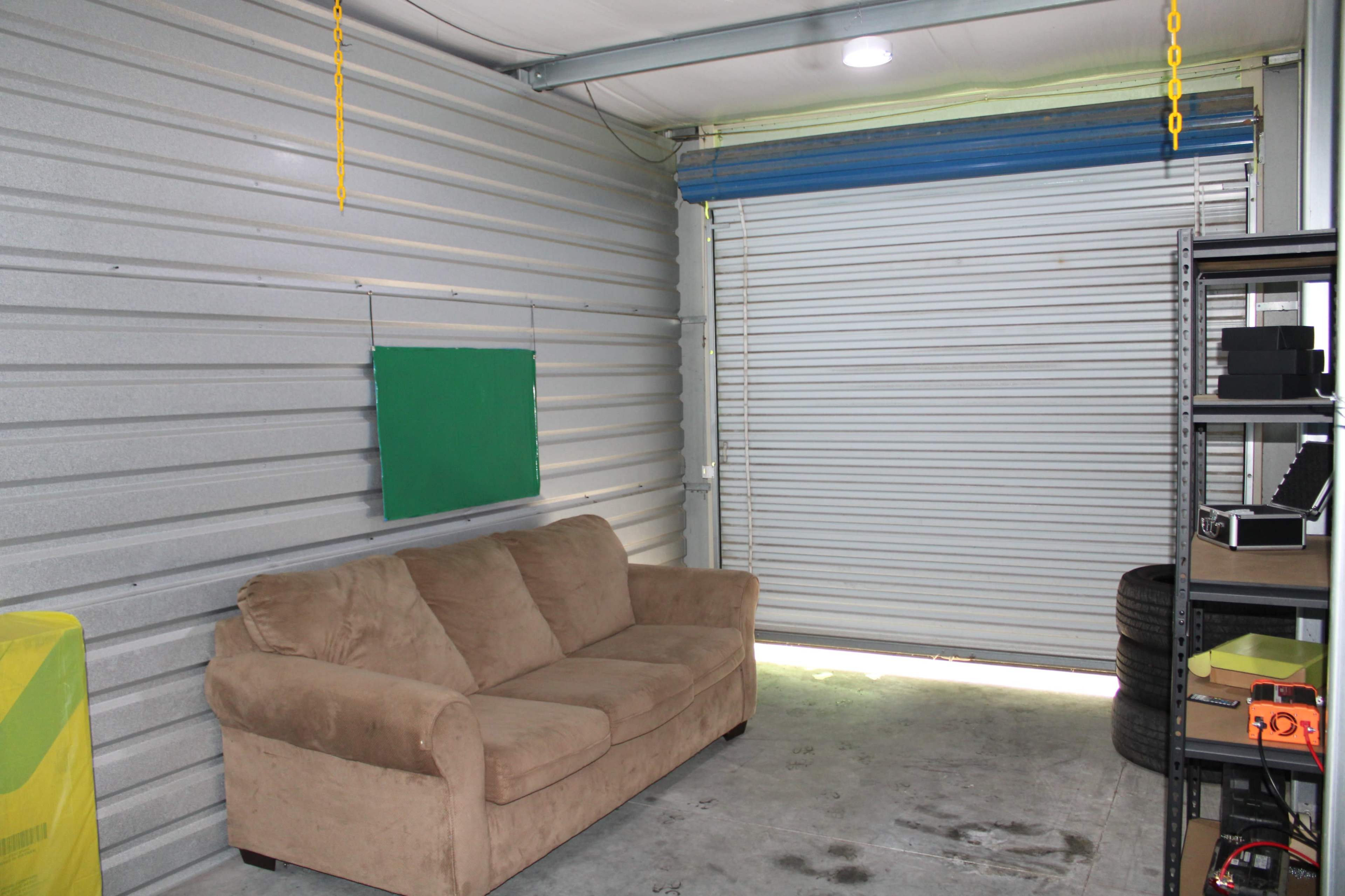 The image shows a storage garage with a beige couch, a green chalkboard mounted on the wall, and a partially open roll-up door letting in light.