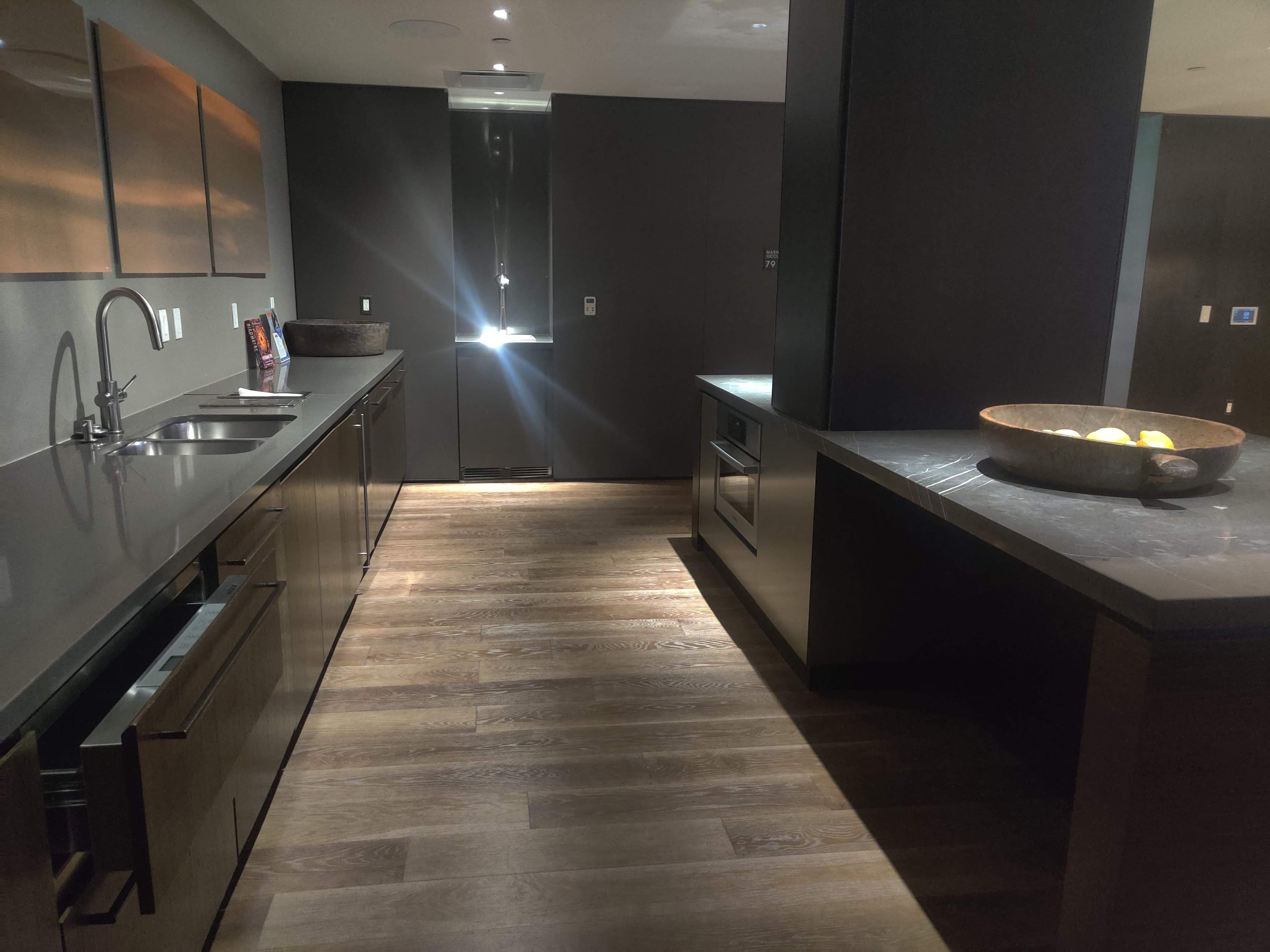 A modern kitchen with dark cabinetry, a large sink, and a countertop featuring a bowl of fruit.