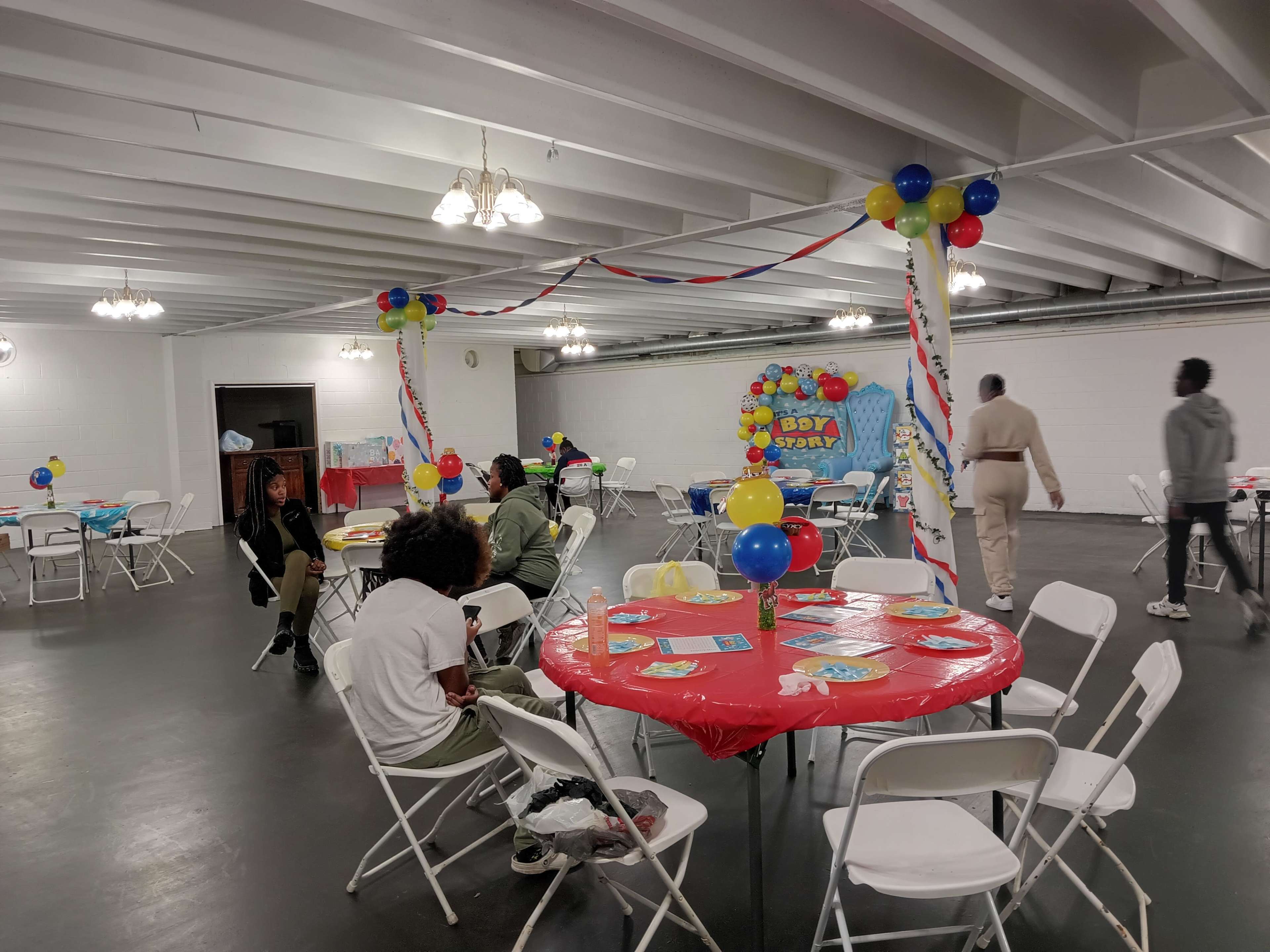 A decorated room with tables covered in red tablecloths, balloons, and a birthday banner, set up for a celebration.