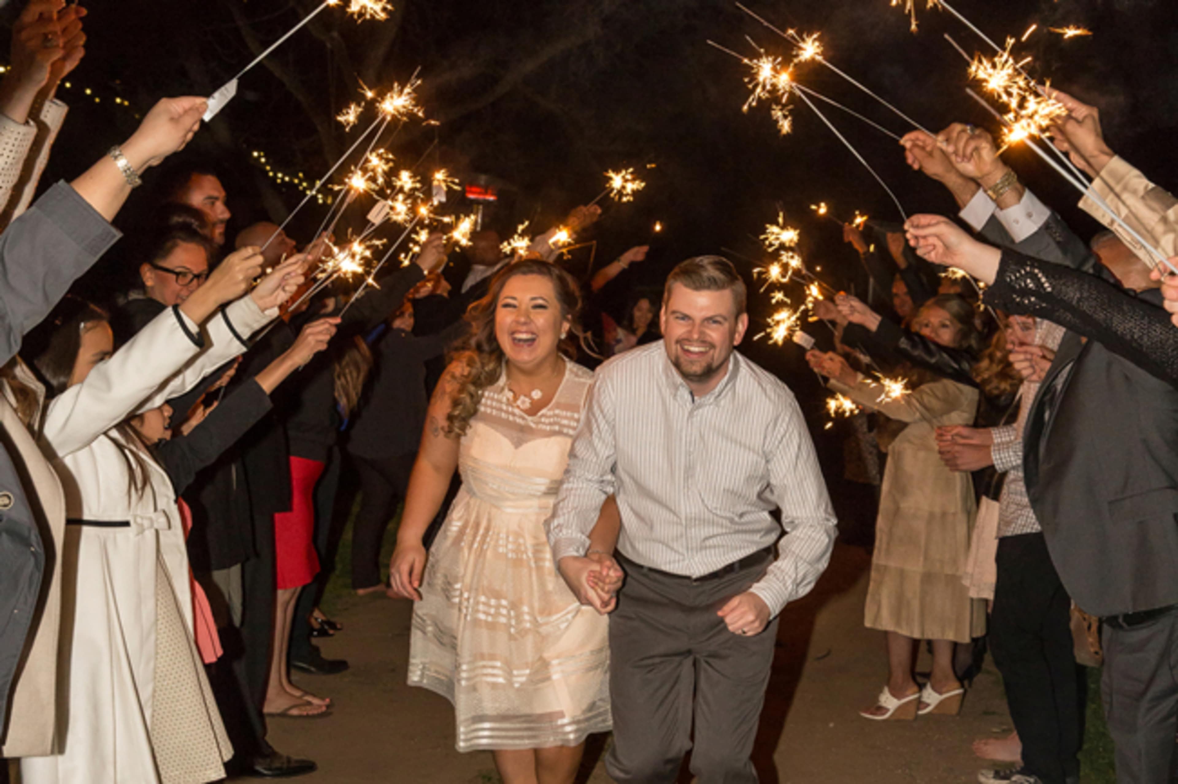 A couple runs through a tunnel of guests holding sparklers in a nighttime celebration.