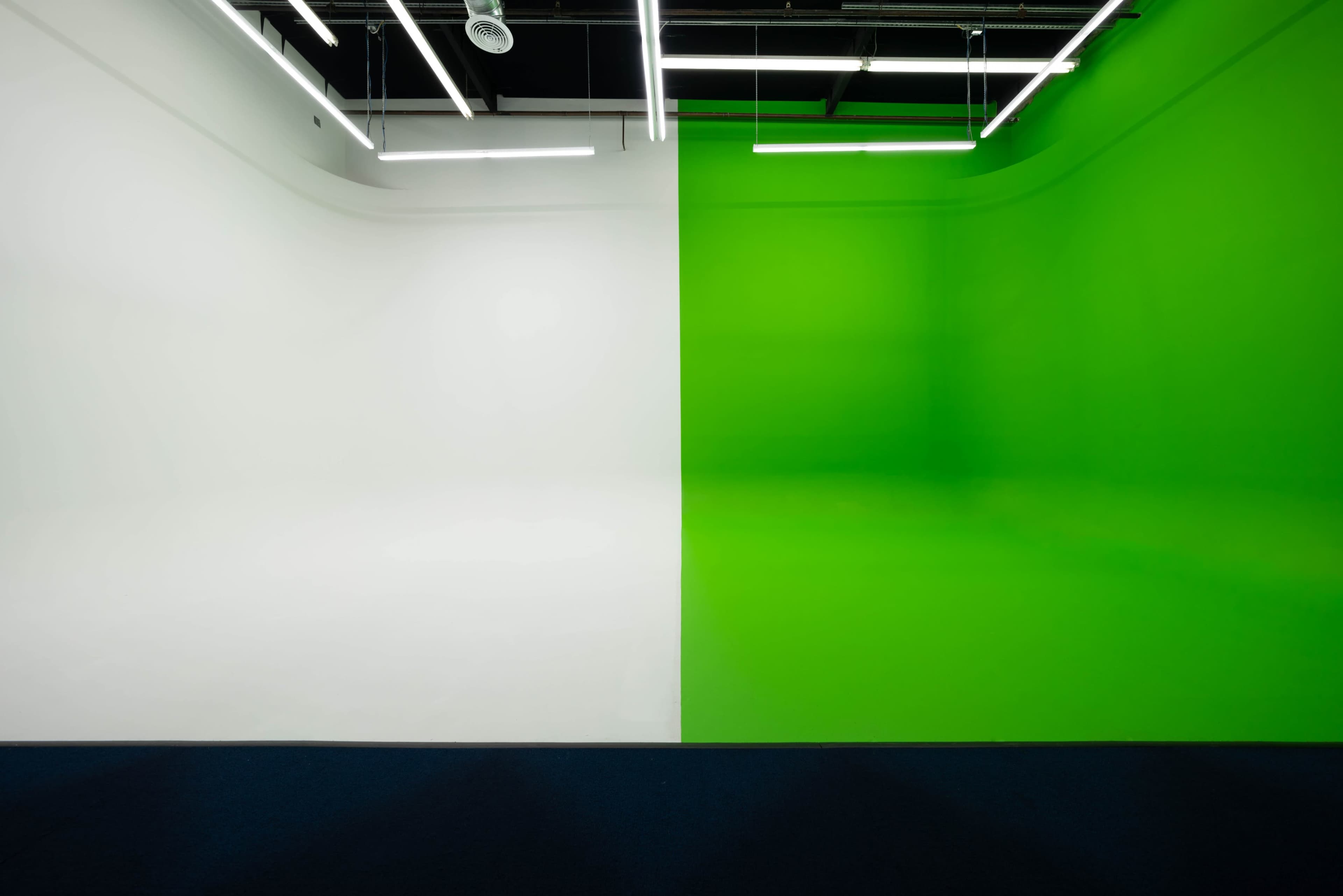 The image shows a split room with one side painted white and the other side painted bright green, illuminated by overhead fluorescent lights.