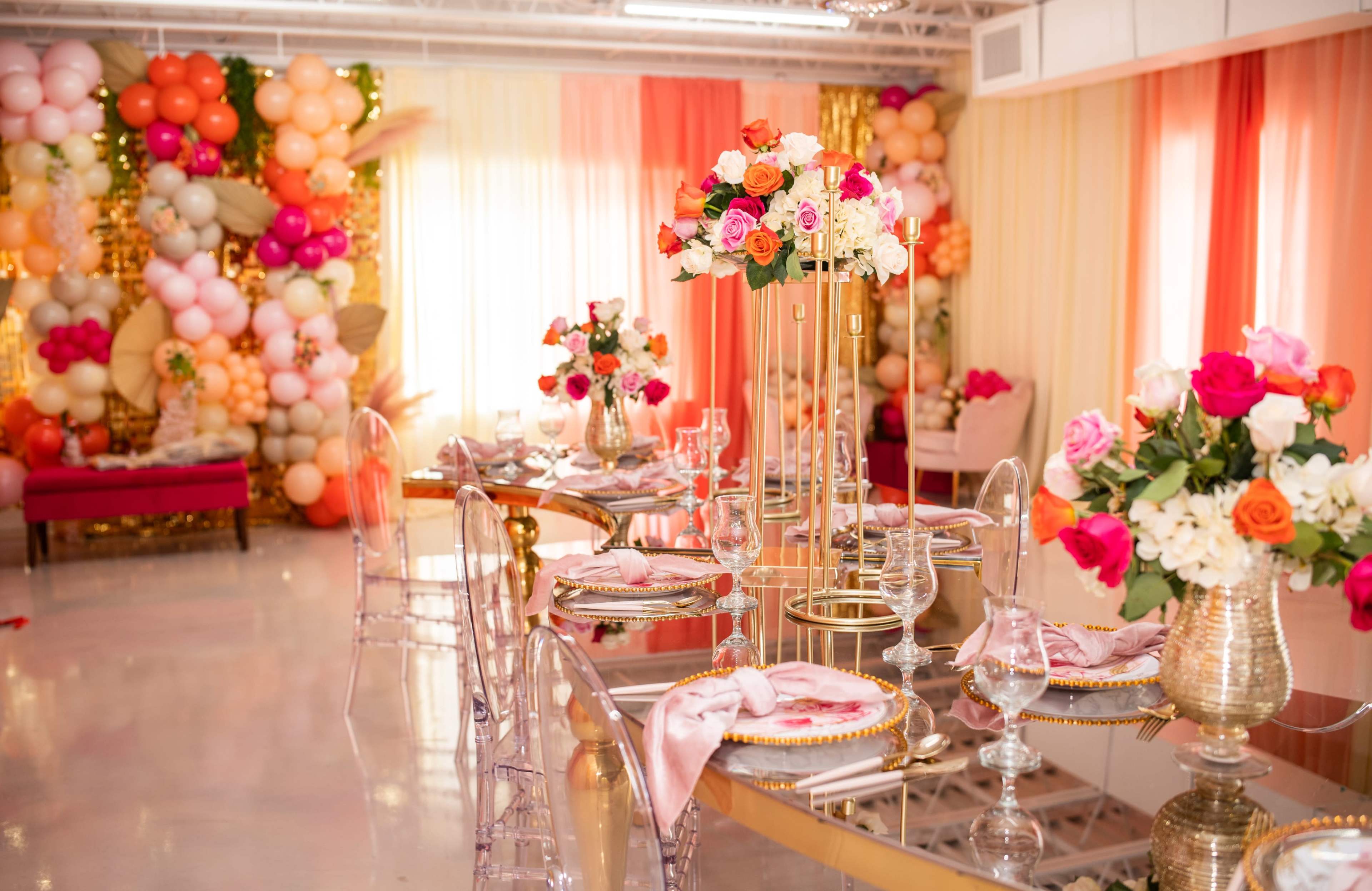 The image features a decorated event space with elegantly arranged tables, floral centerpieces, and colorful balloon displays in the background.