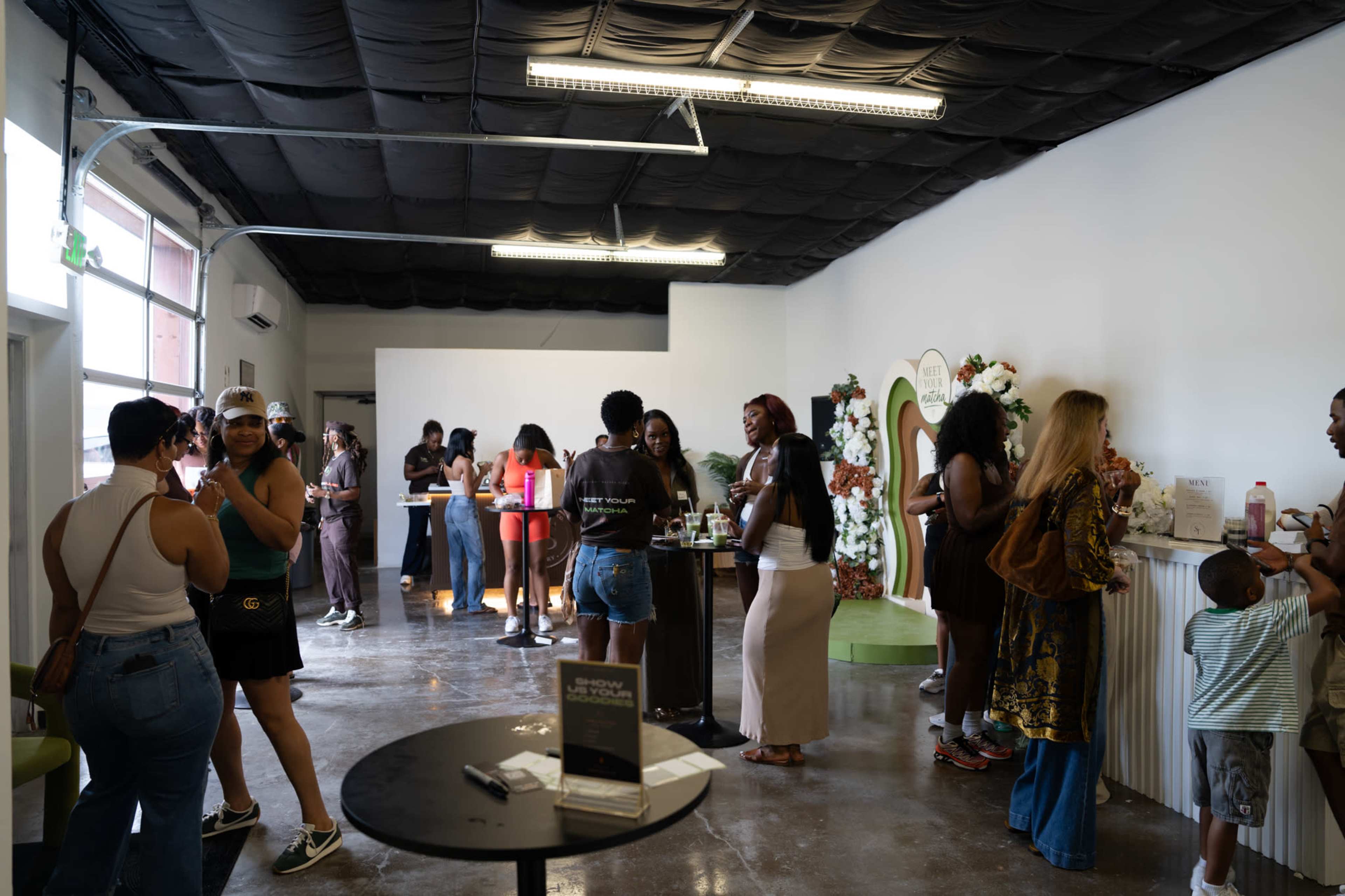 A group of people is socializing and enjoying refreshments in a modern, open space with floral decorations and standing tables.