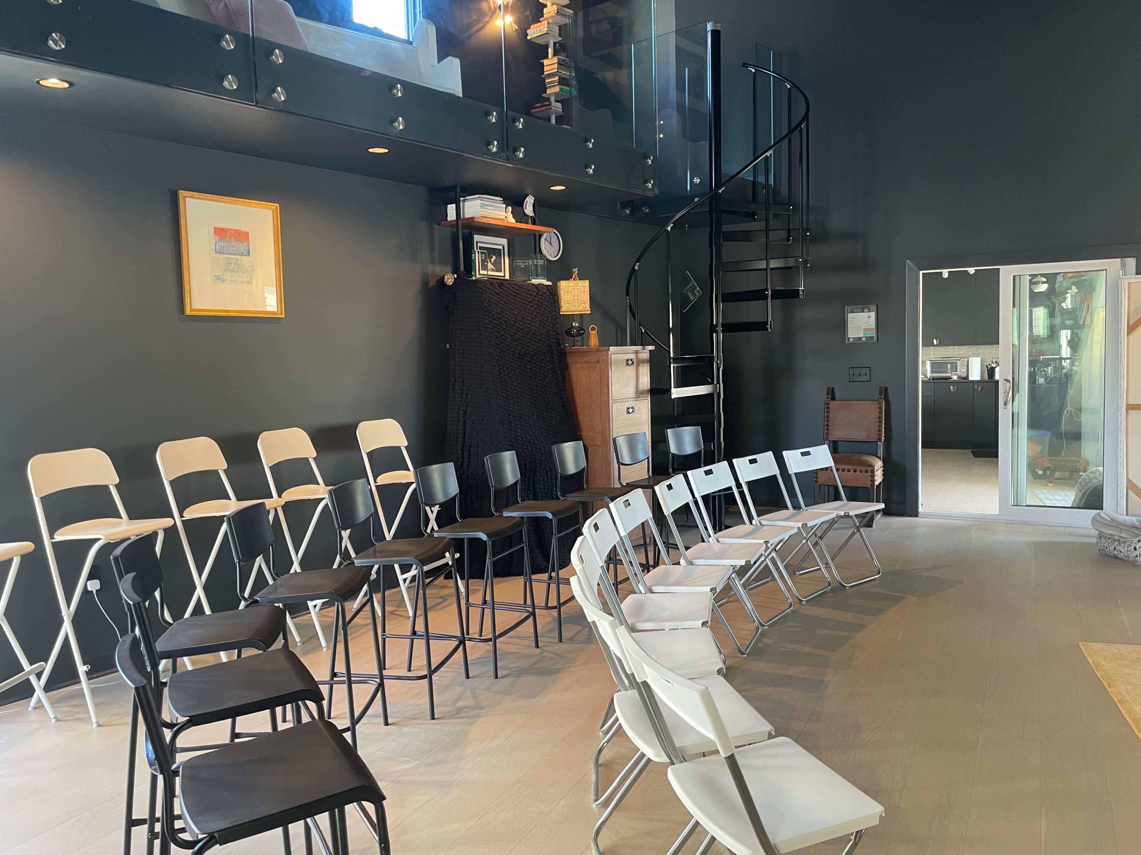 A room with a spiral staircase, featuring a semi-circle of folding chairs in various colors arranged on the floor.