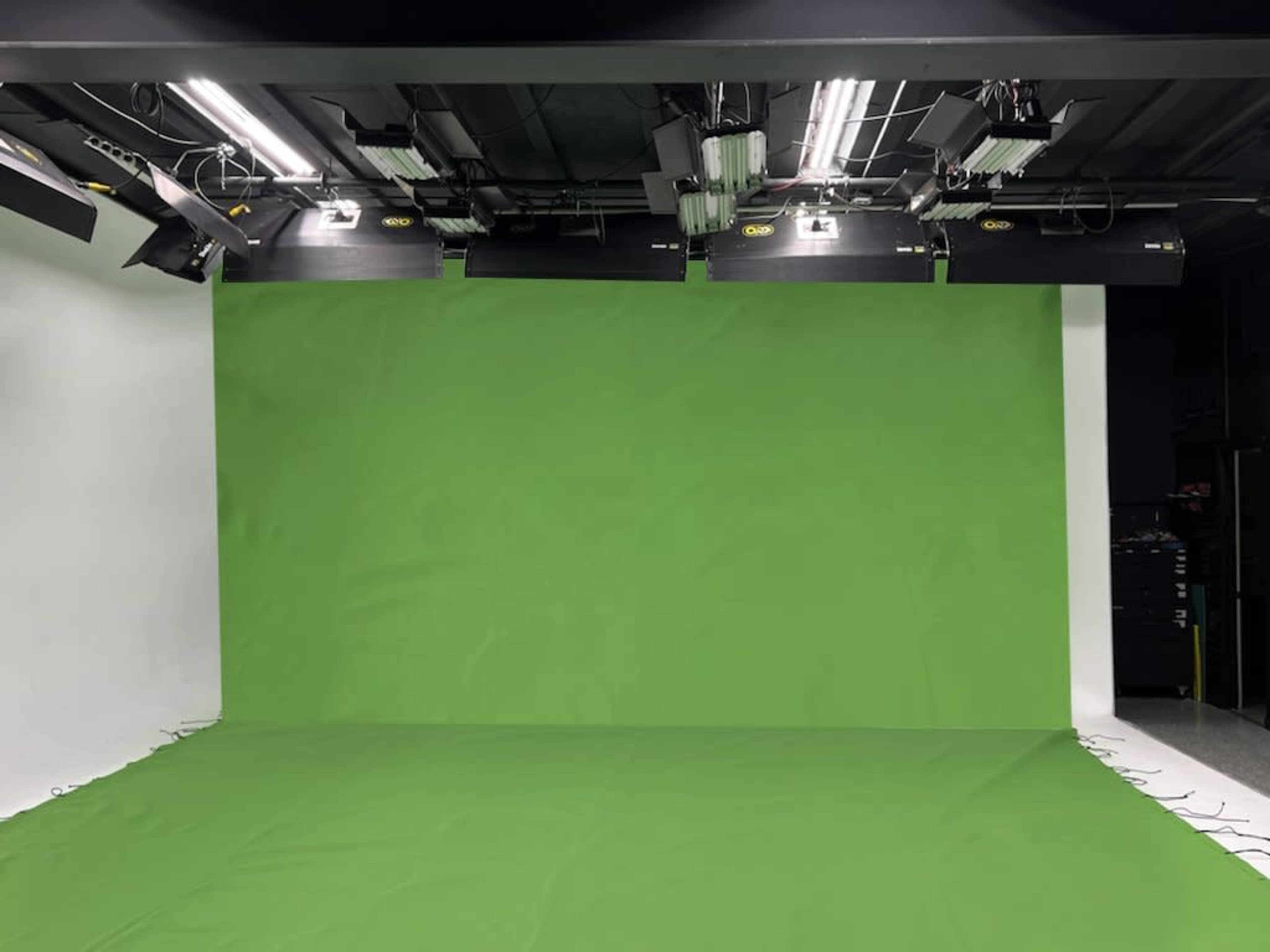 The image shows a studio setup featuring a green screen backdrop with overhead lighting equipment.