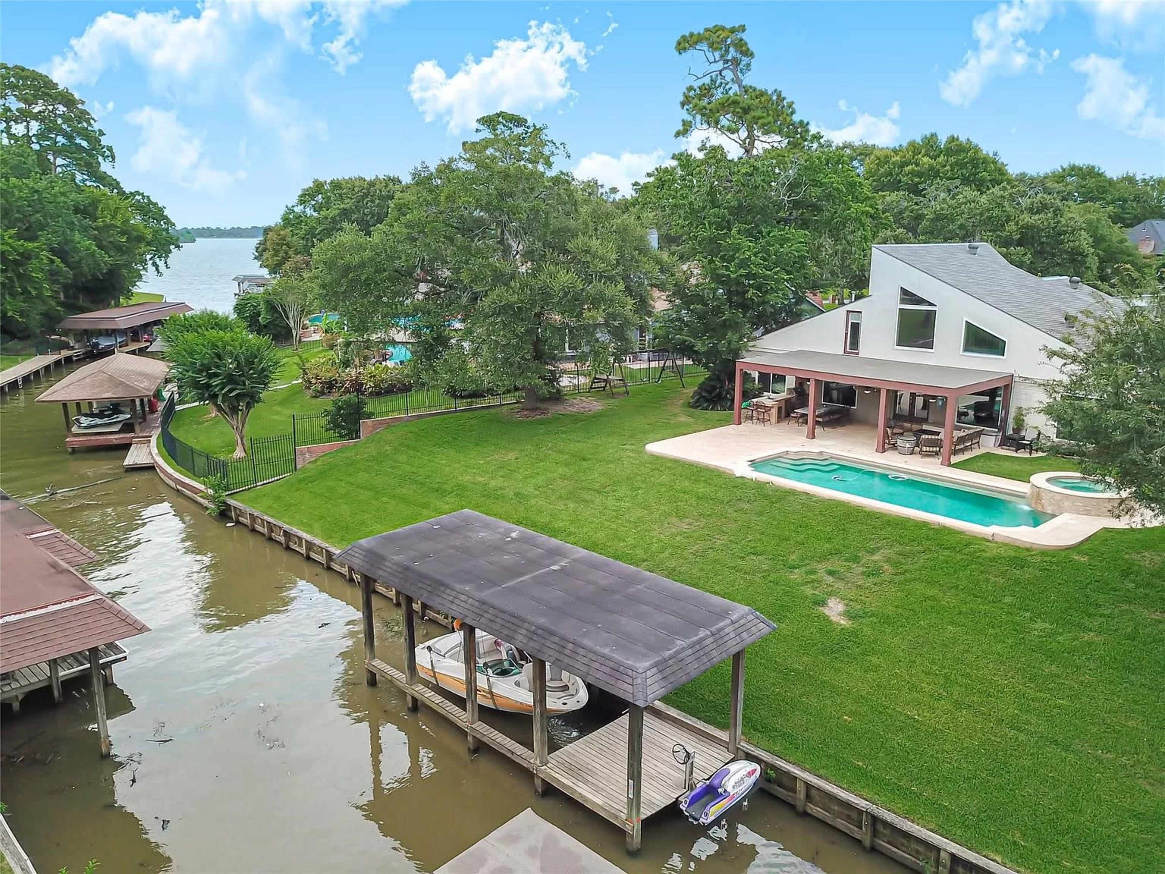 A spacious yard with a swimming pool and a canal leading to a body of water, surrounded by trees and residential buildings.