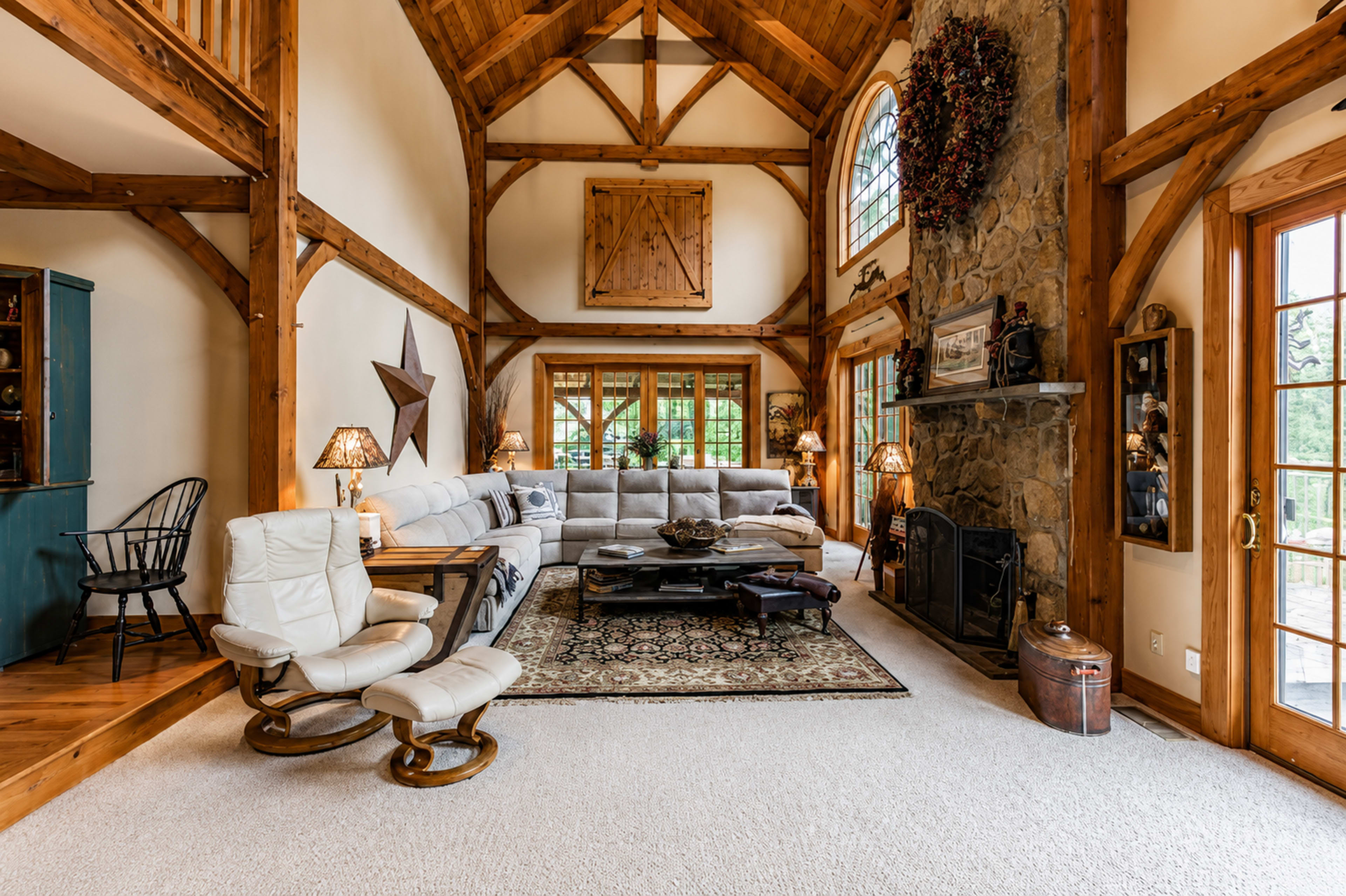 The spacious living room features a high wood-beamed ceiling, a stone fireplace, and a large sectional sofa arranged around a coffee table.