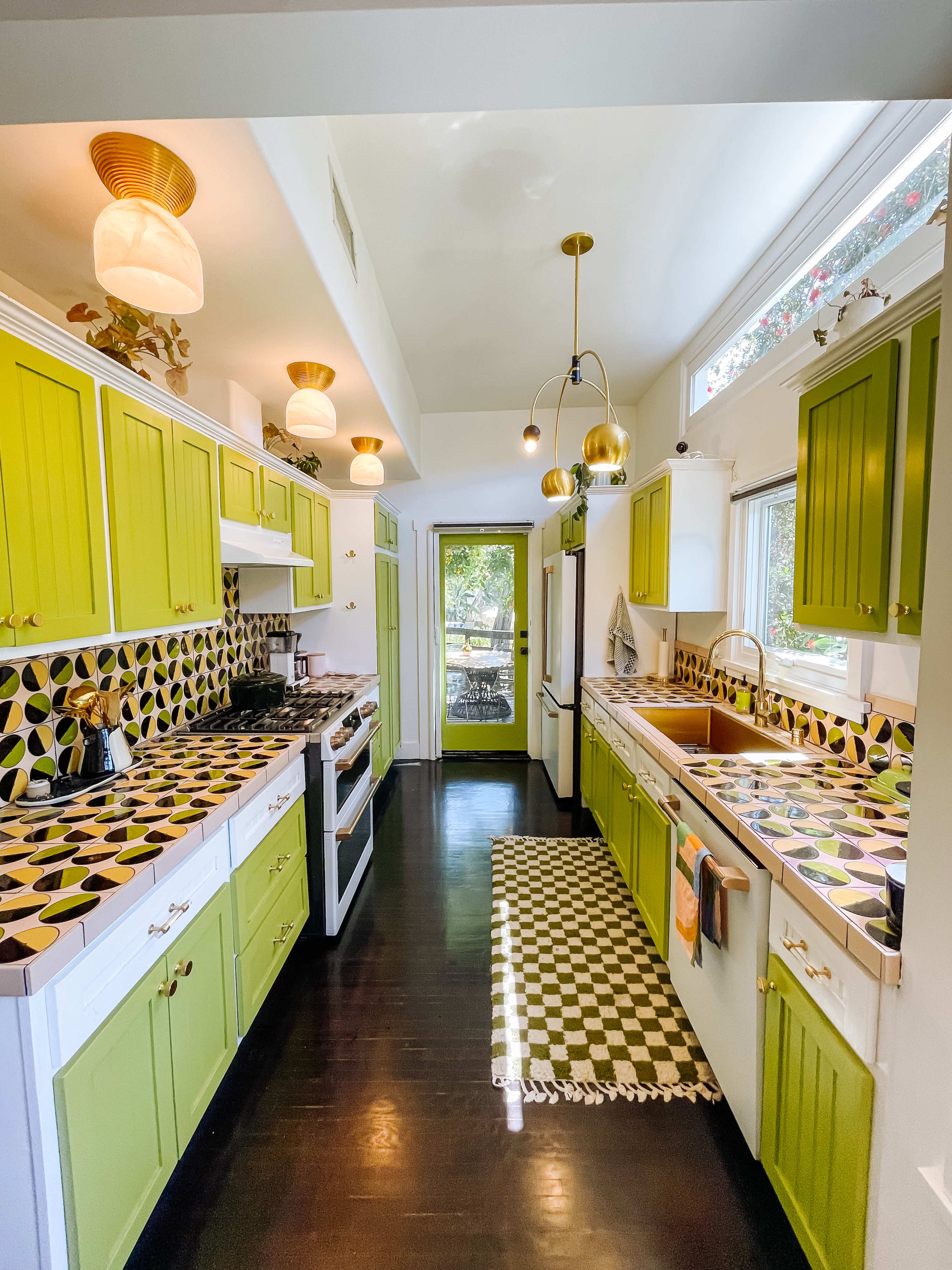 The kitchen features bright green cabinets, geometric patterned countertops, and a combination of pendant and wall lights.
