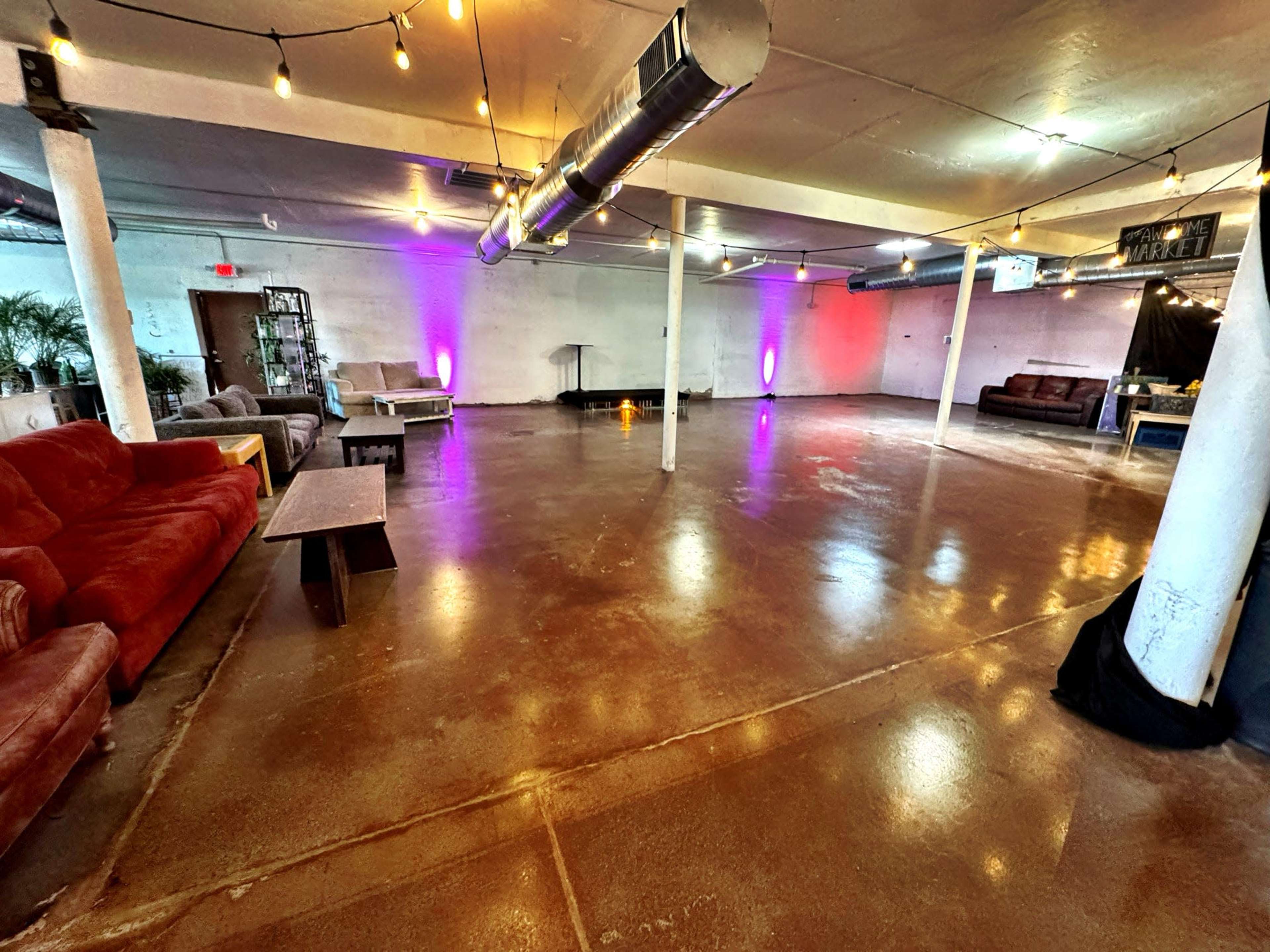 The image shows a spacious room with a polished concrete floor, various seating arrangements, and colorful lighting along the walls.