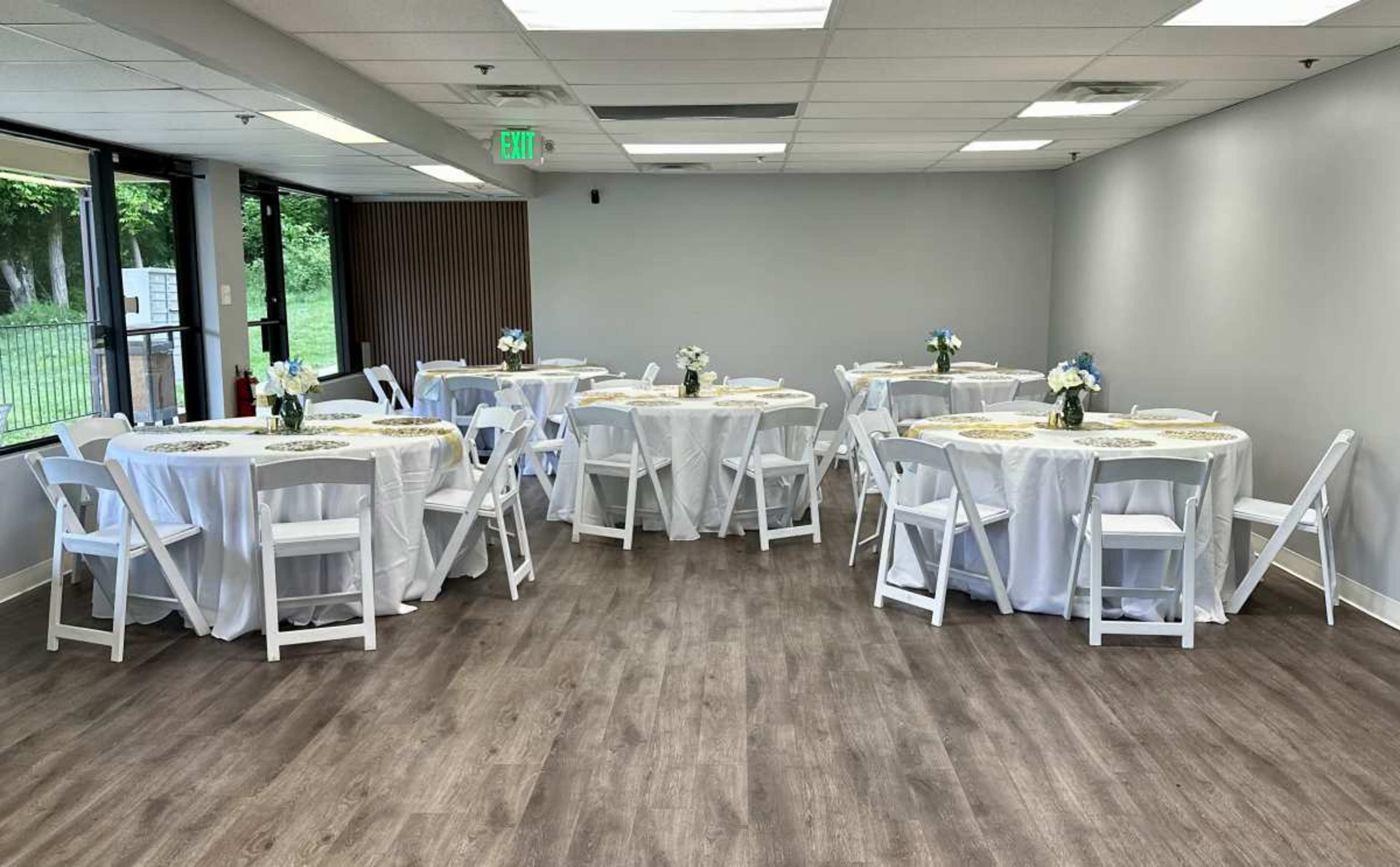 The image shows a large indoor space with several round tables covered in white tablecloths, each adorned with small floral centerpieces.