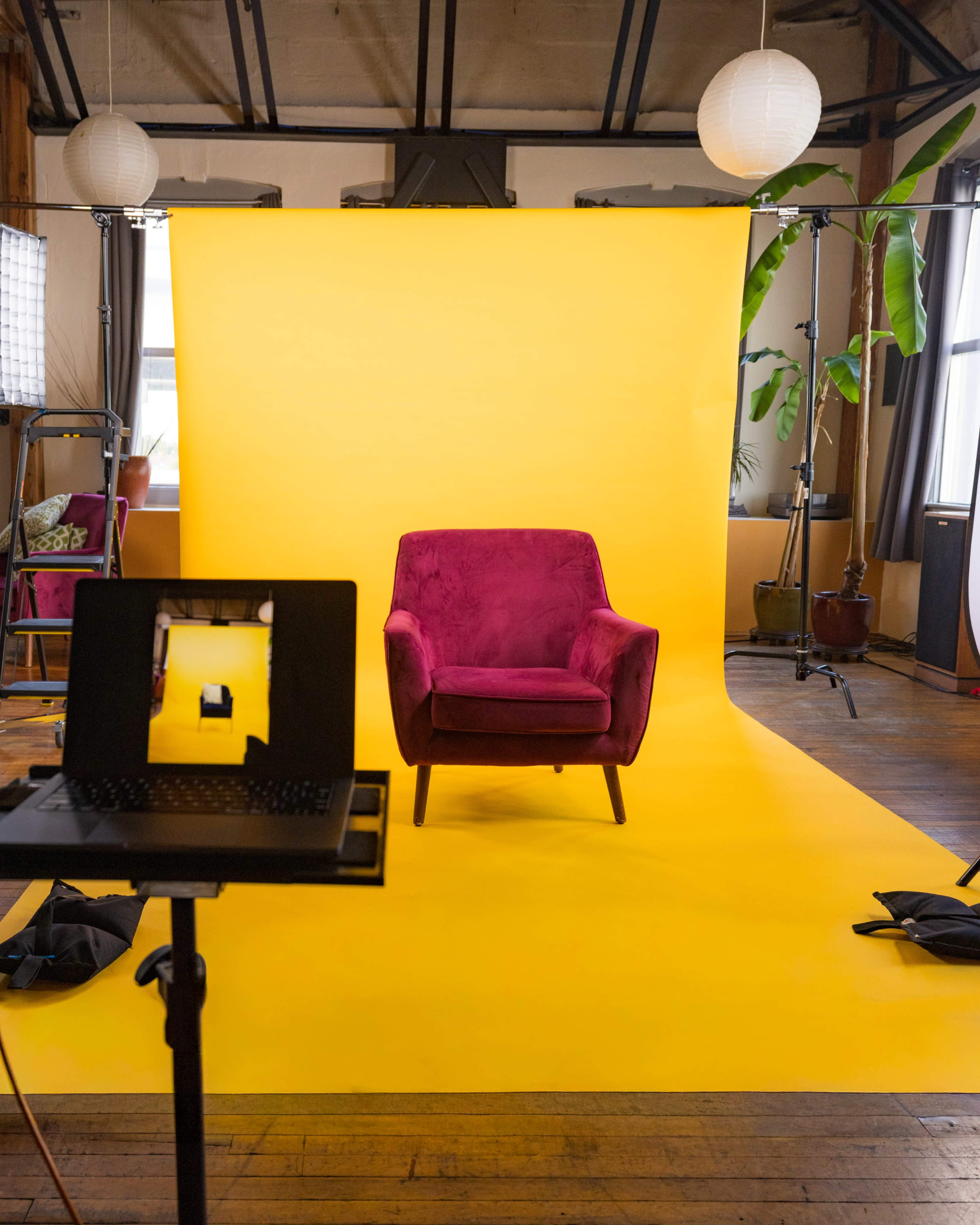 A magenta armchair is positioned against a vibrant yellow backdrop in a well-lit studio.