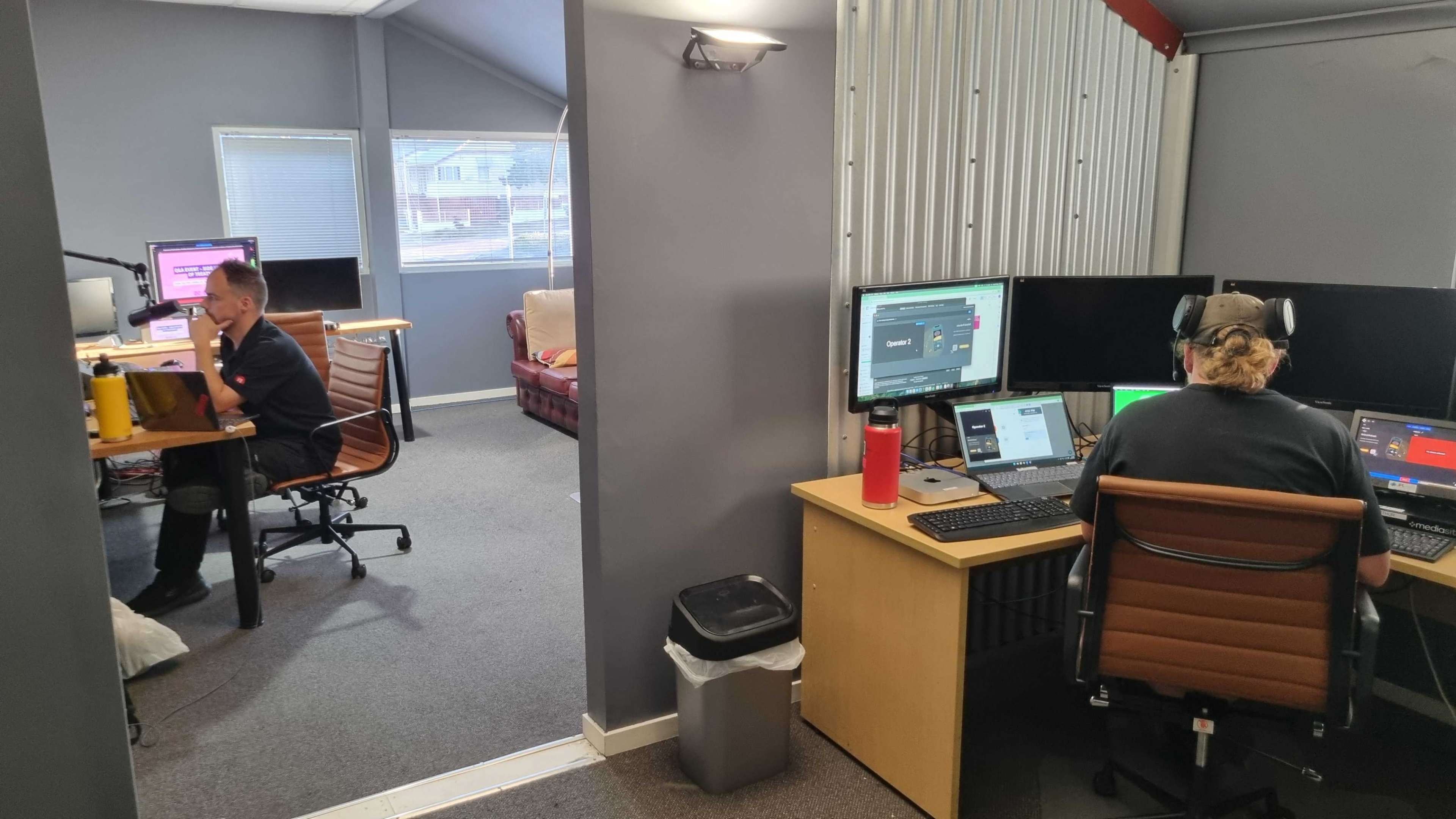 The image shows an office space with two workstations, one occupied by a person sitting at a desk with multiple monitors.