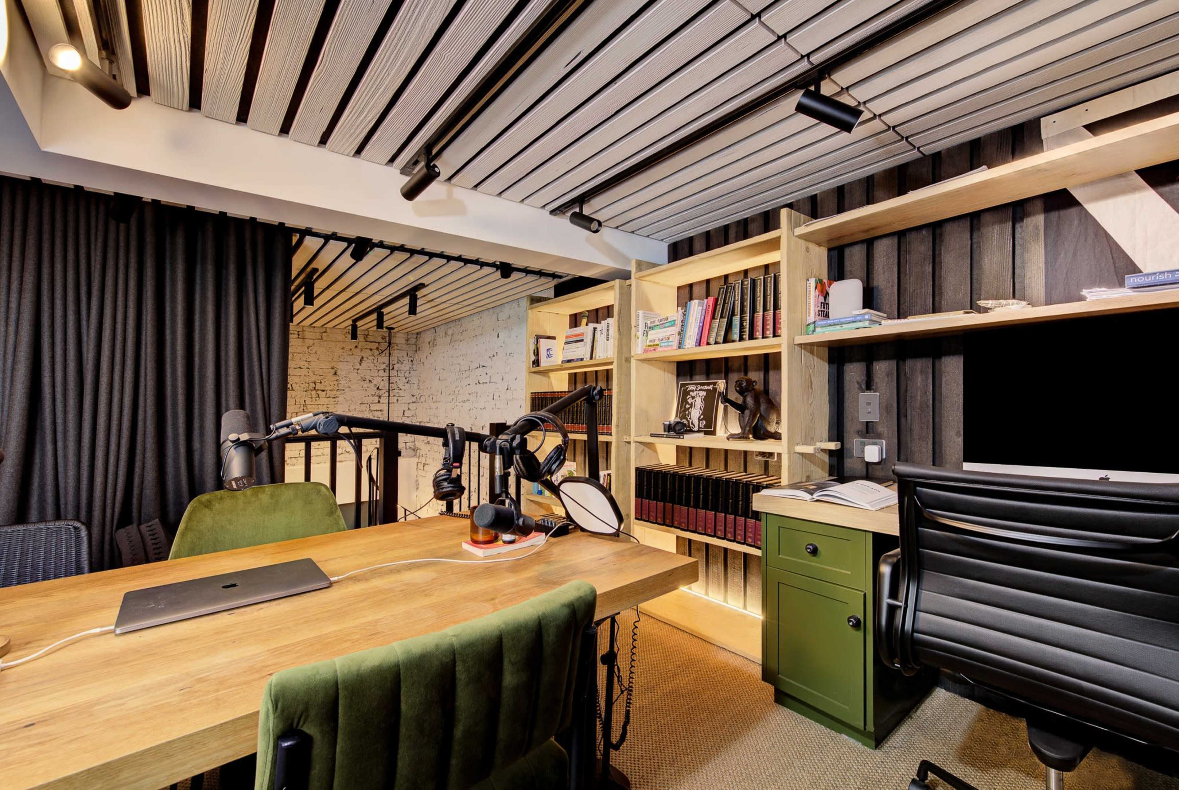 The image shows a modern office space featuring a wooden desk with a computer, green chair, shelves filled with books, and a black curtain.