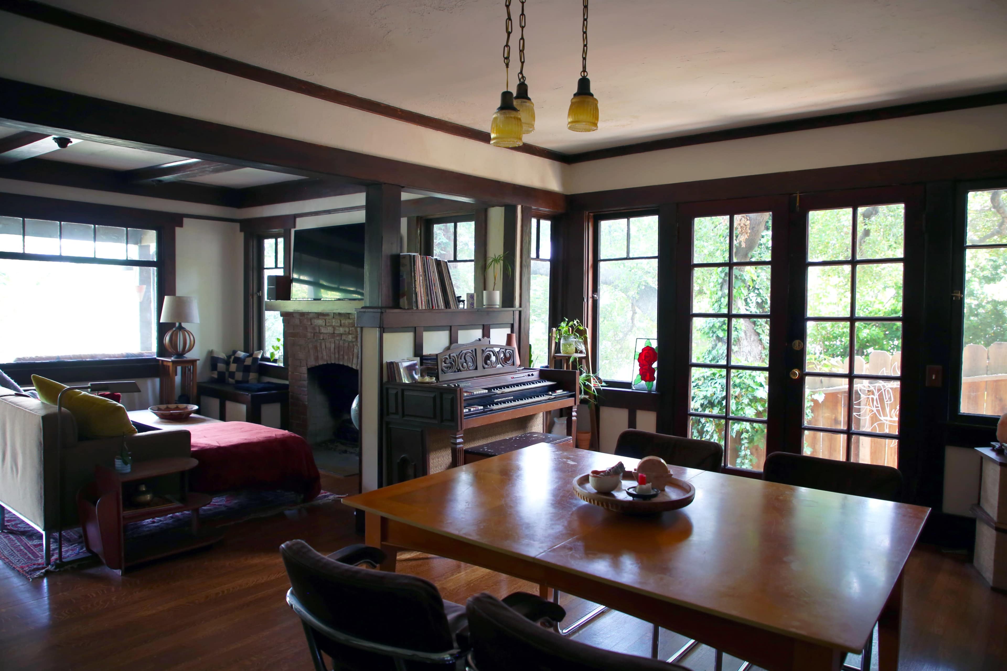 A cozy living room with a fireplace, a dining table, a piano, and large windows allowing light to stream in.