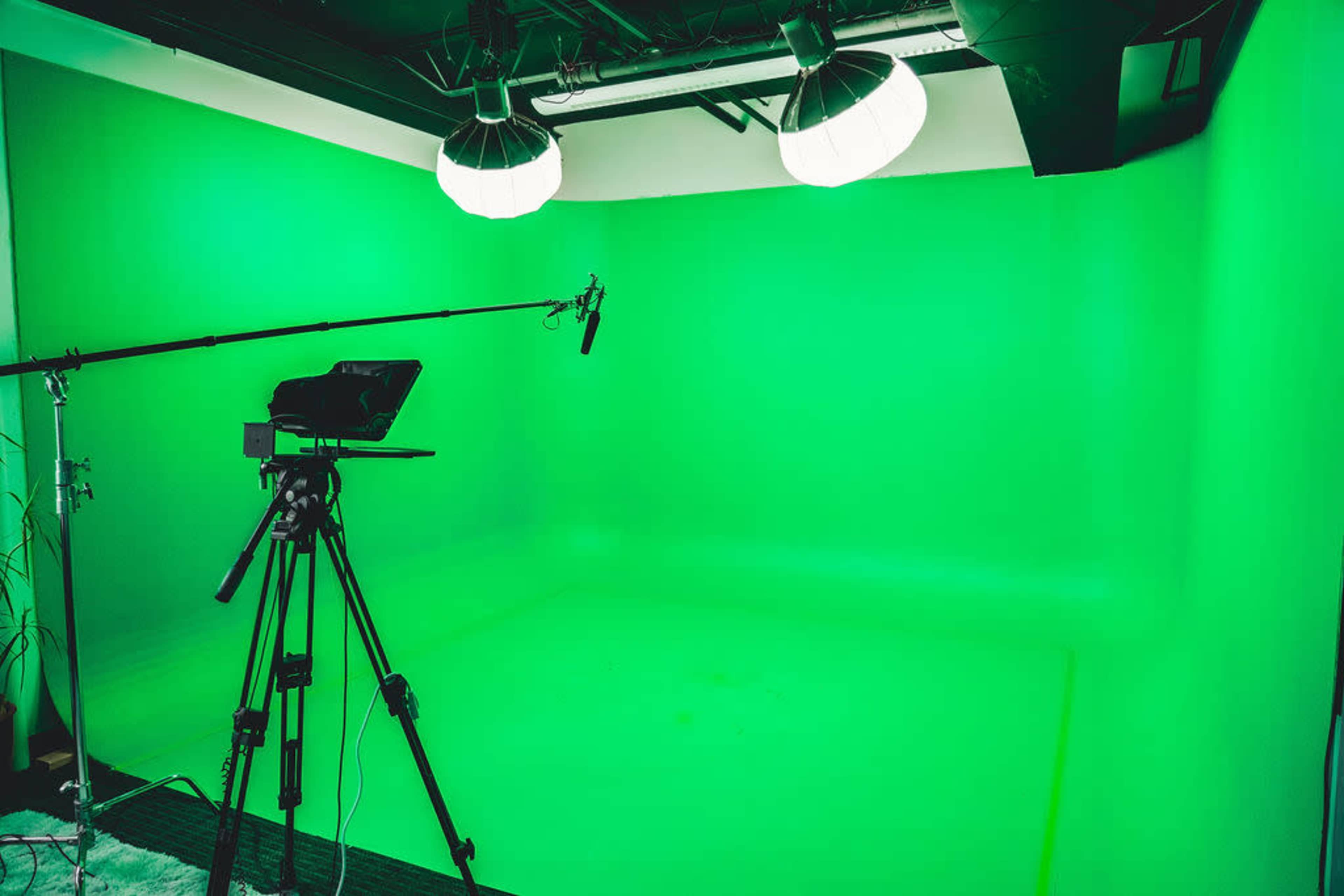 A green screen studio with a camera, microphone, and lighting setup.
