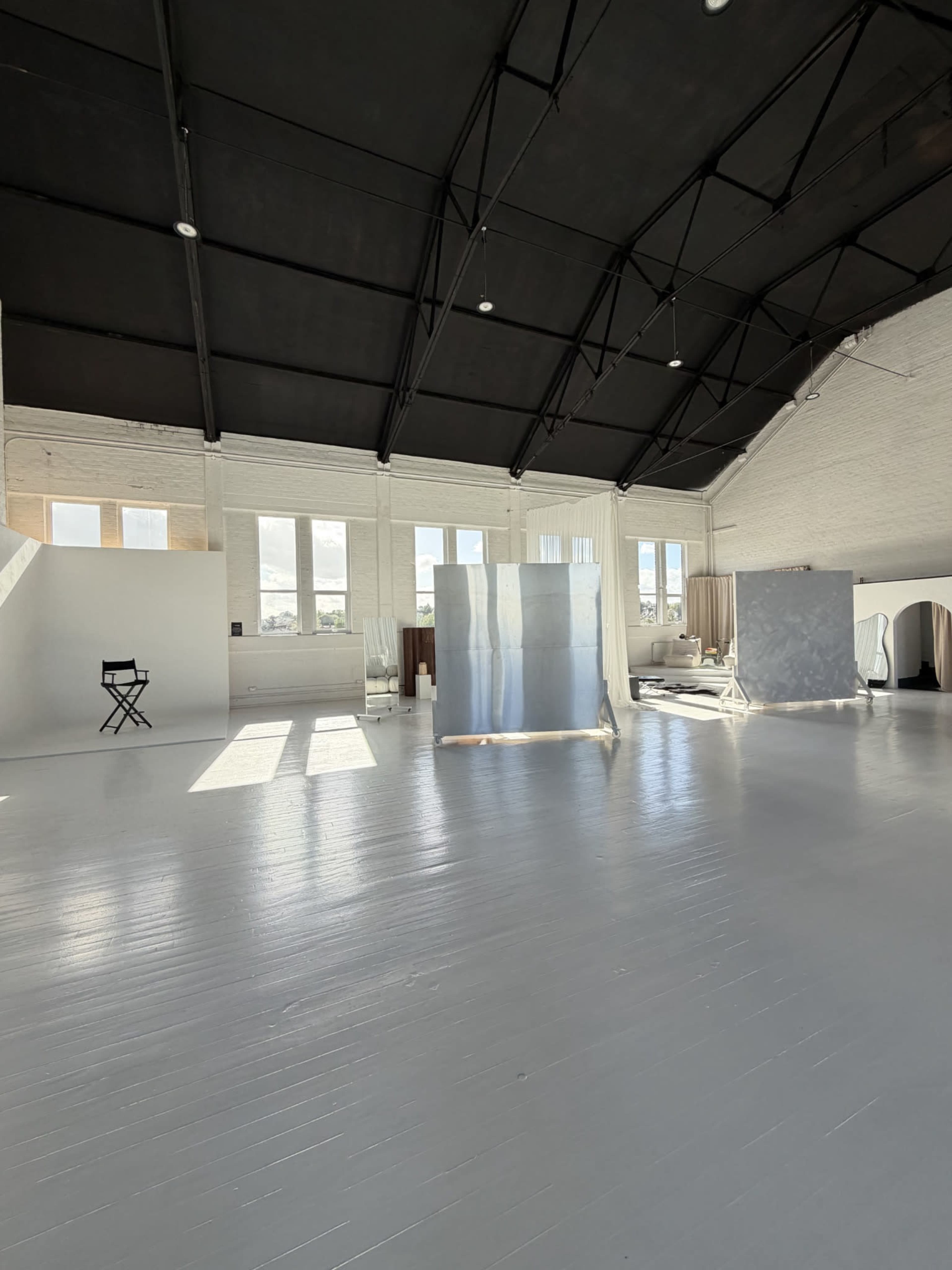 The image shows a spacious, well-lit studio with a high black ceiling and several white panels scattered throughout the room.