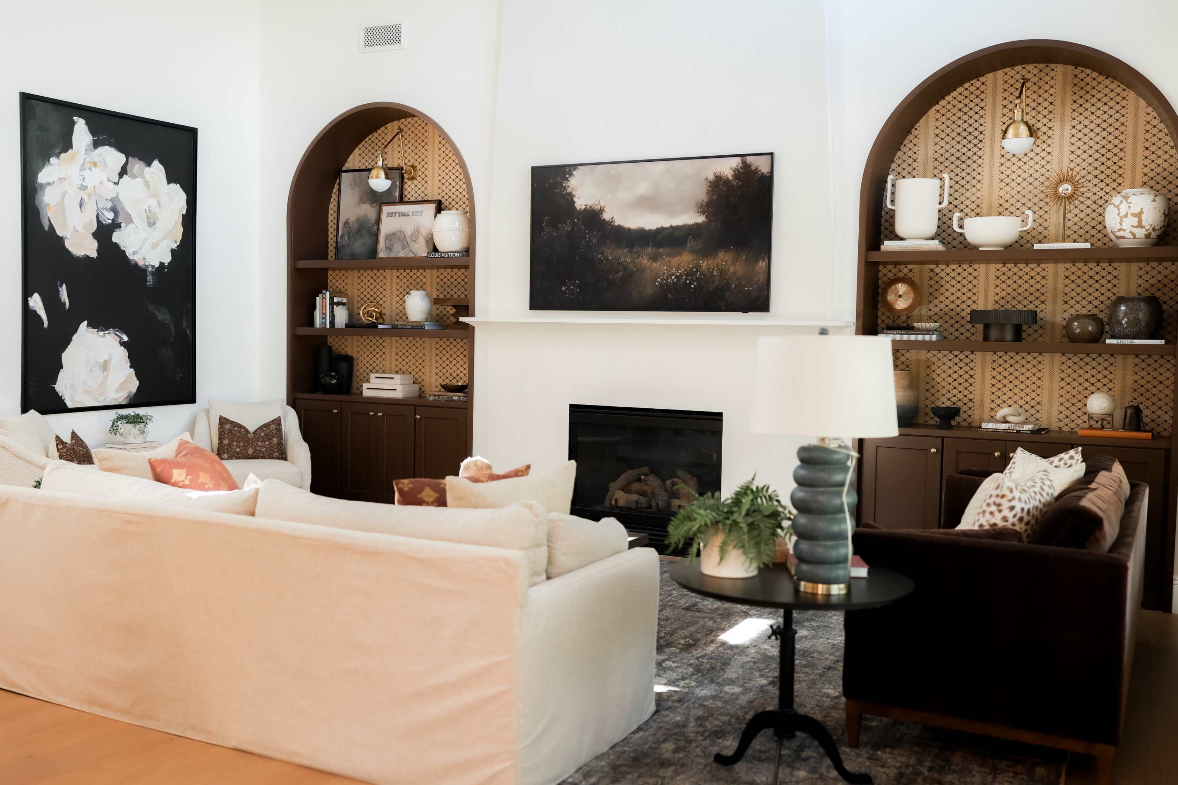 The image shows a stylish living room with a fireplace, two sofas, and decorative shelves featuring various objects and artwork on the walls.