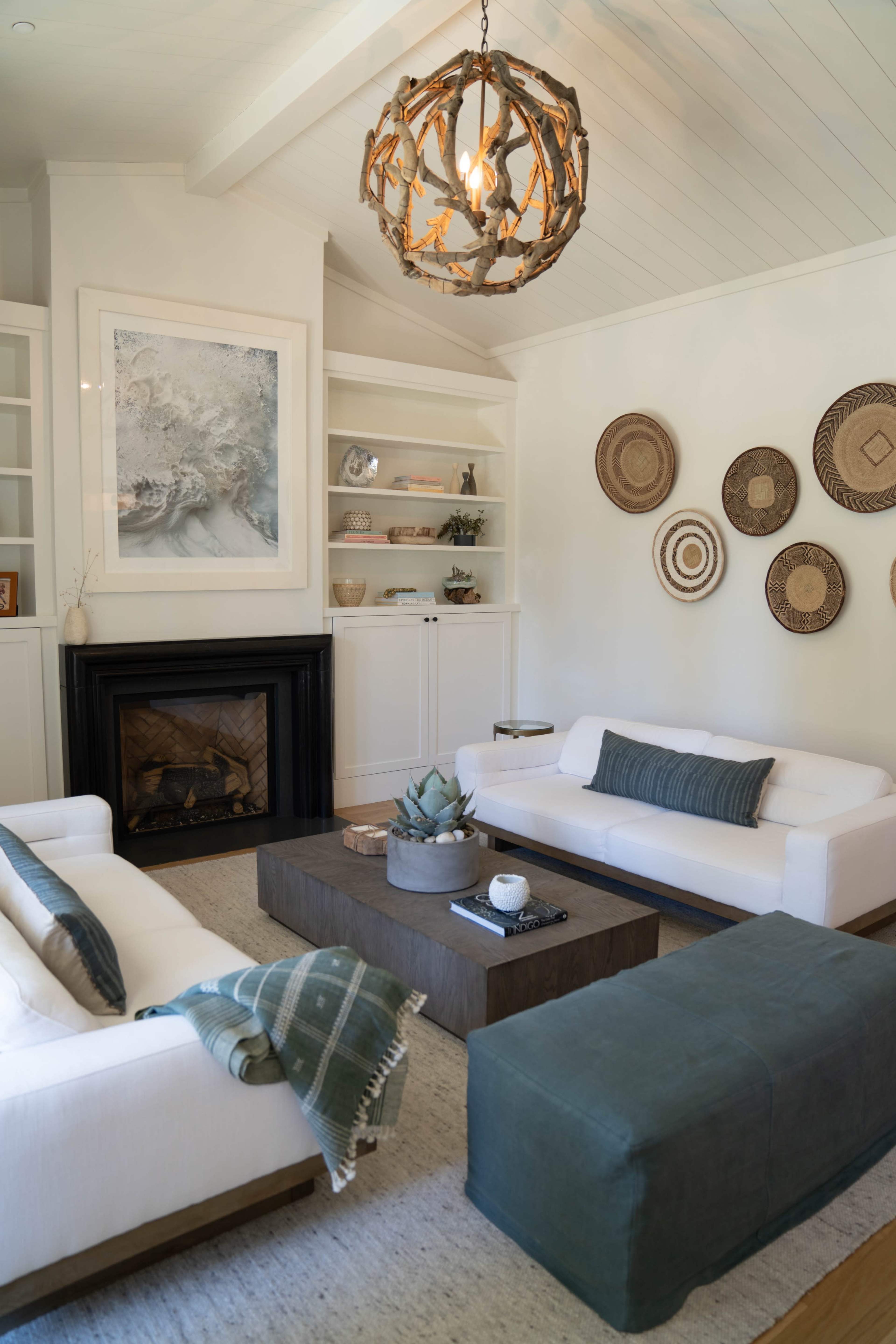 A modern living room features two white sofas, a wooden coffee table, a fireplace, and decorative wall hangings.
