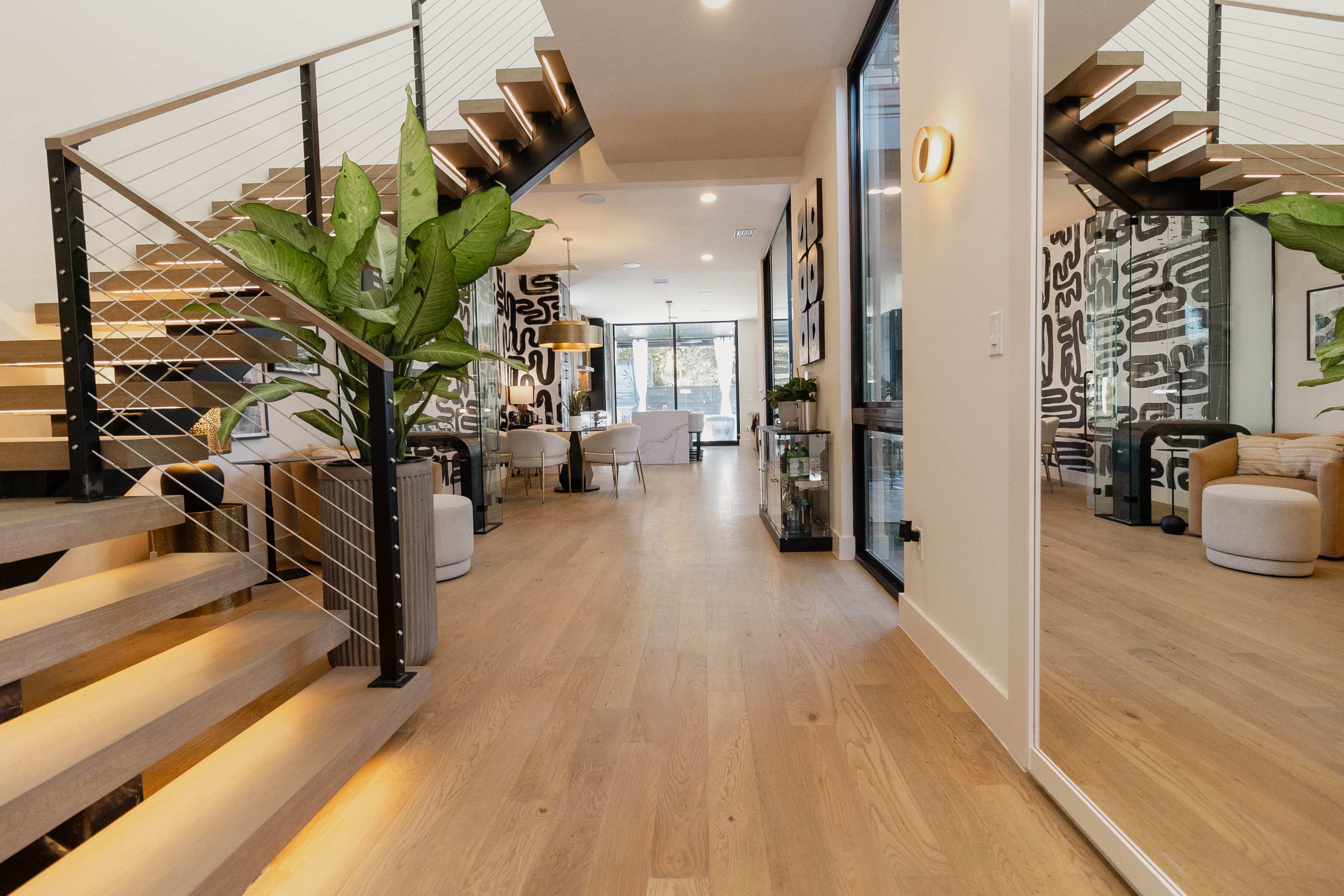A modern interior features a staircase with wooden steps, leading to a spacious living area adorned with a large plant and contemporary furniture.
