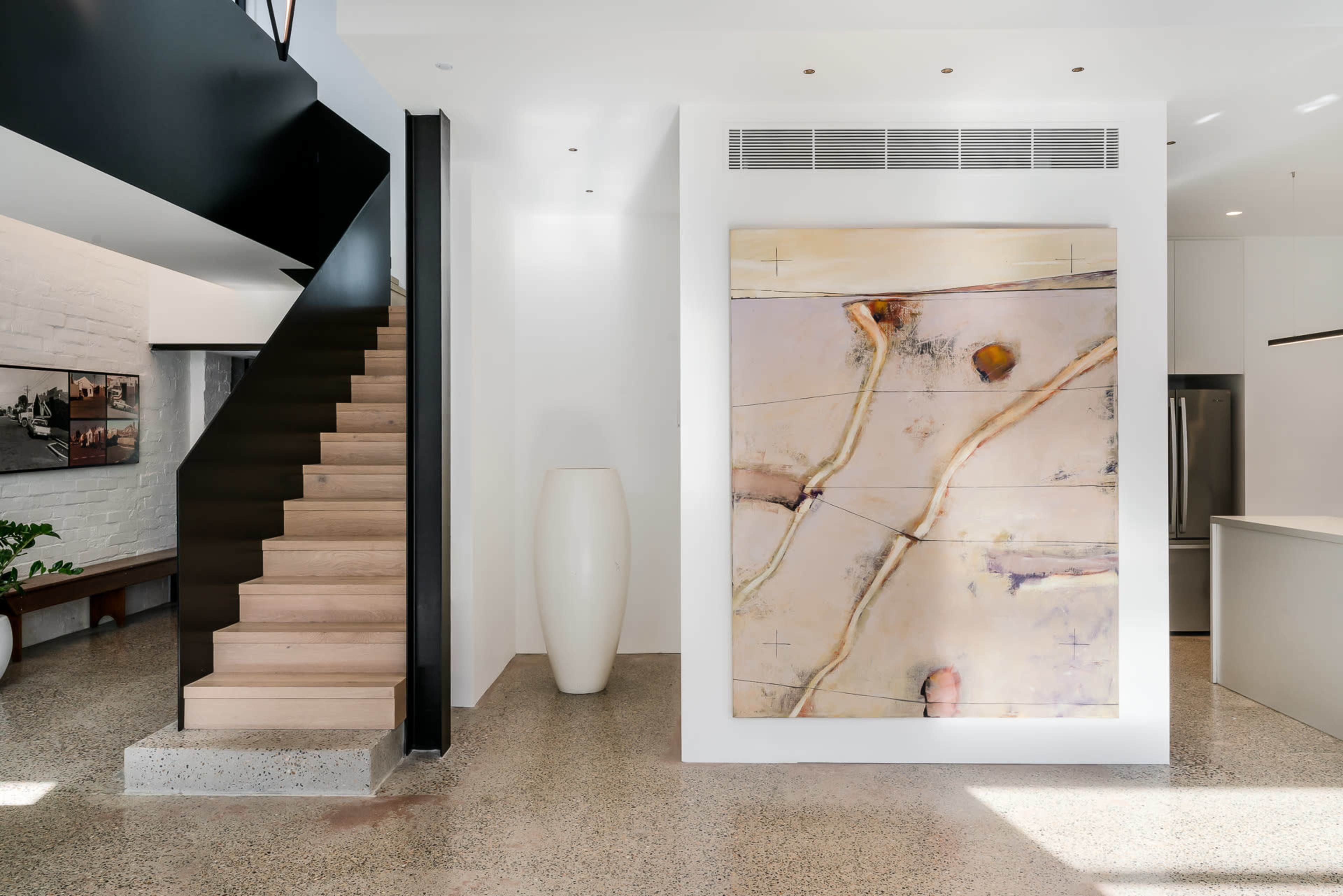 A modern interior with a staircase, a large artwork on the wall, and a minimalistic vase positioned near the stairs.
