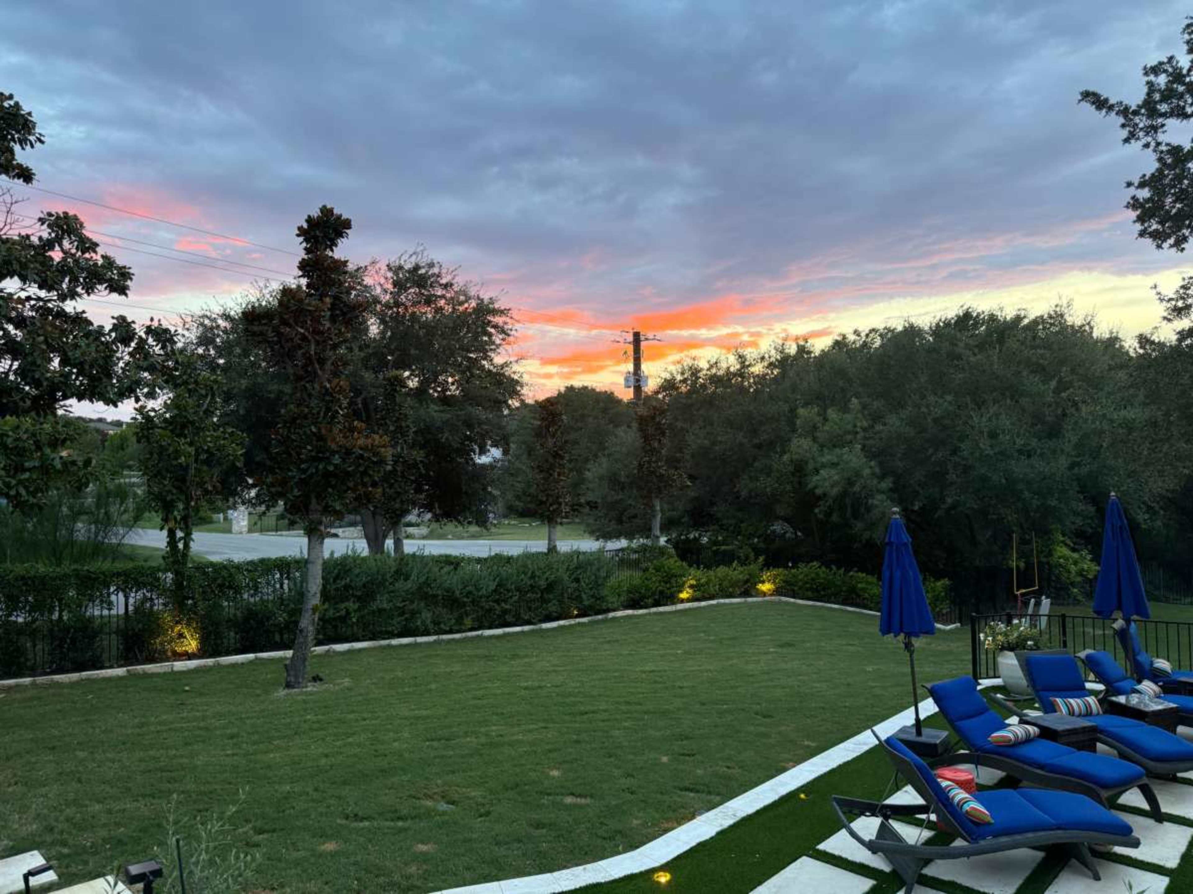 The image shows a backyard with green grass, lounge chairs, and a sunset in the background.