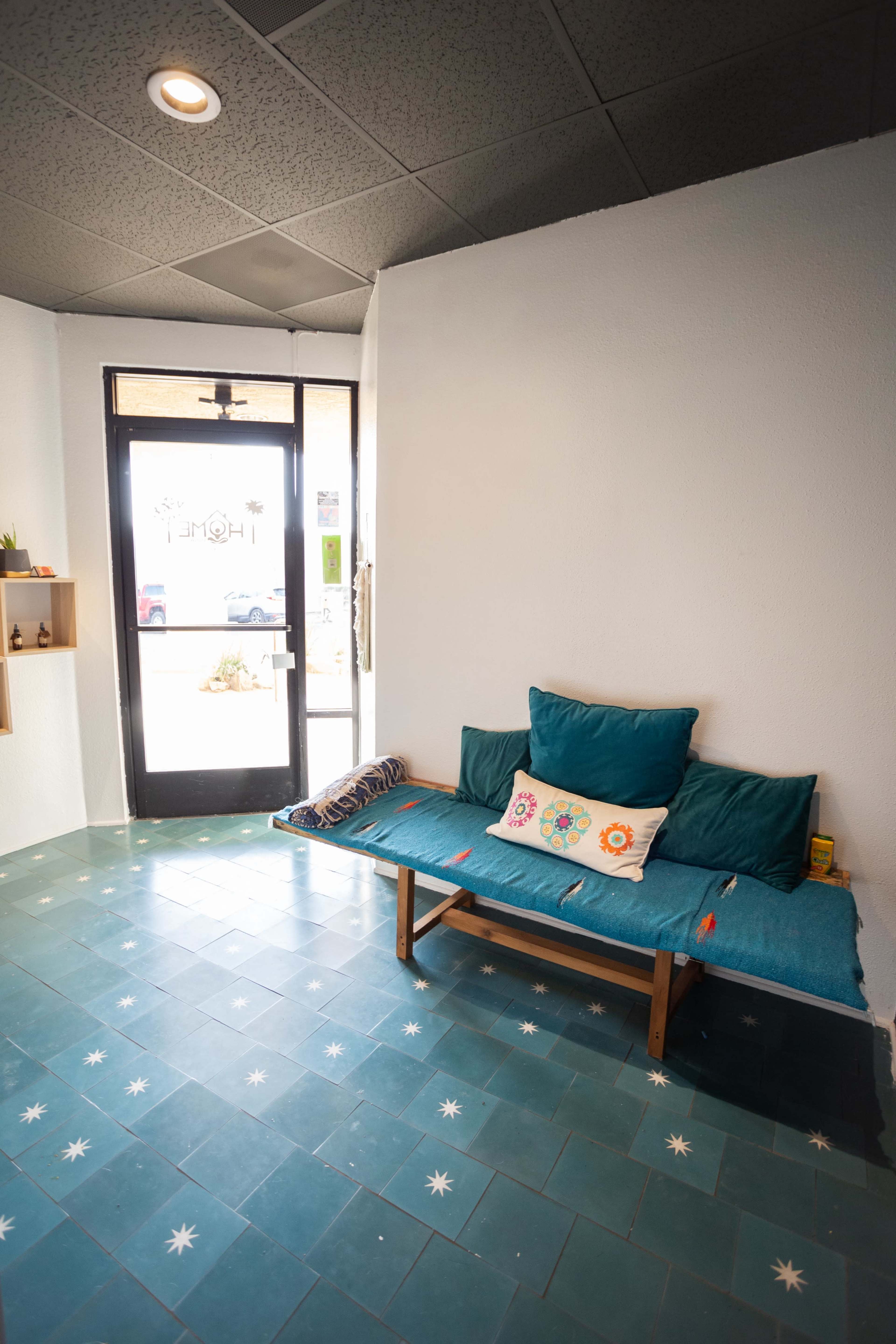 A small interior space featuring a wooden bench with teal cushions, a decorative pillow, and a door leading outside.