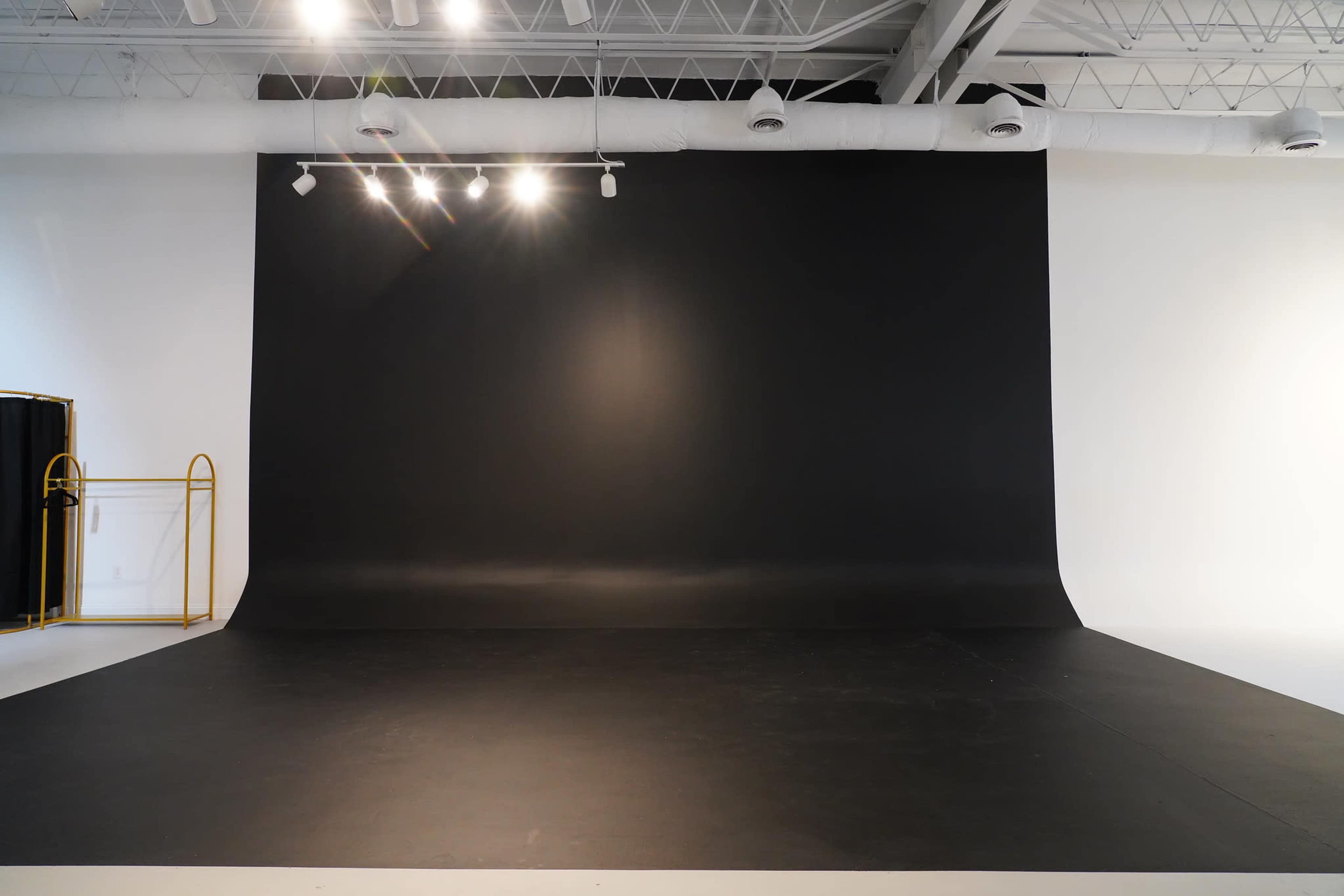 The image shows a photography studio with a large black backdrop and a smooth black floor, illuminated by overhead lights.