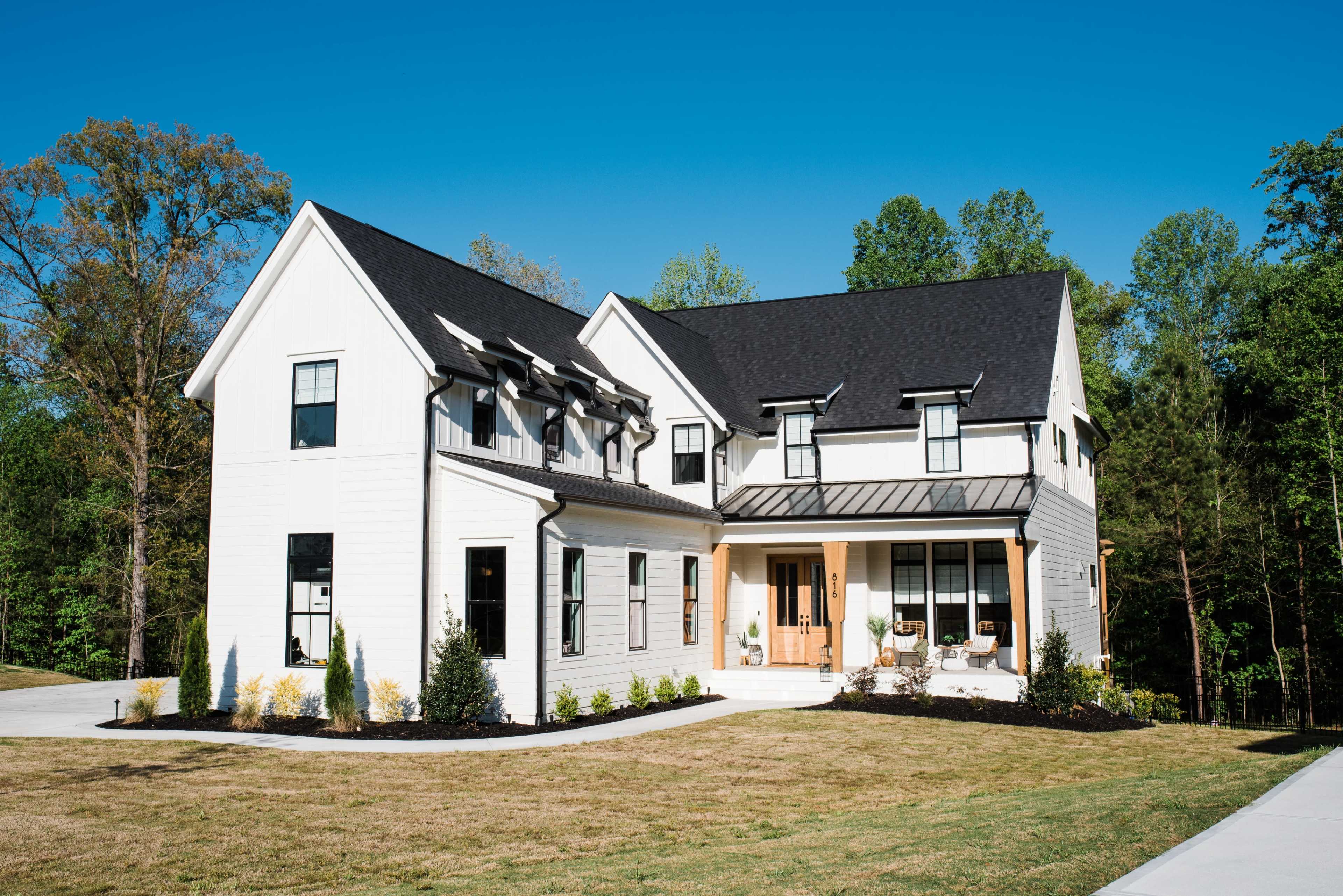 A modern two-story house with a black roof and white siding is set in a landscaped yard.