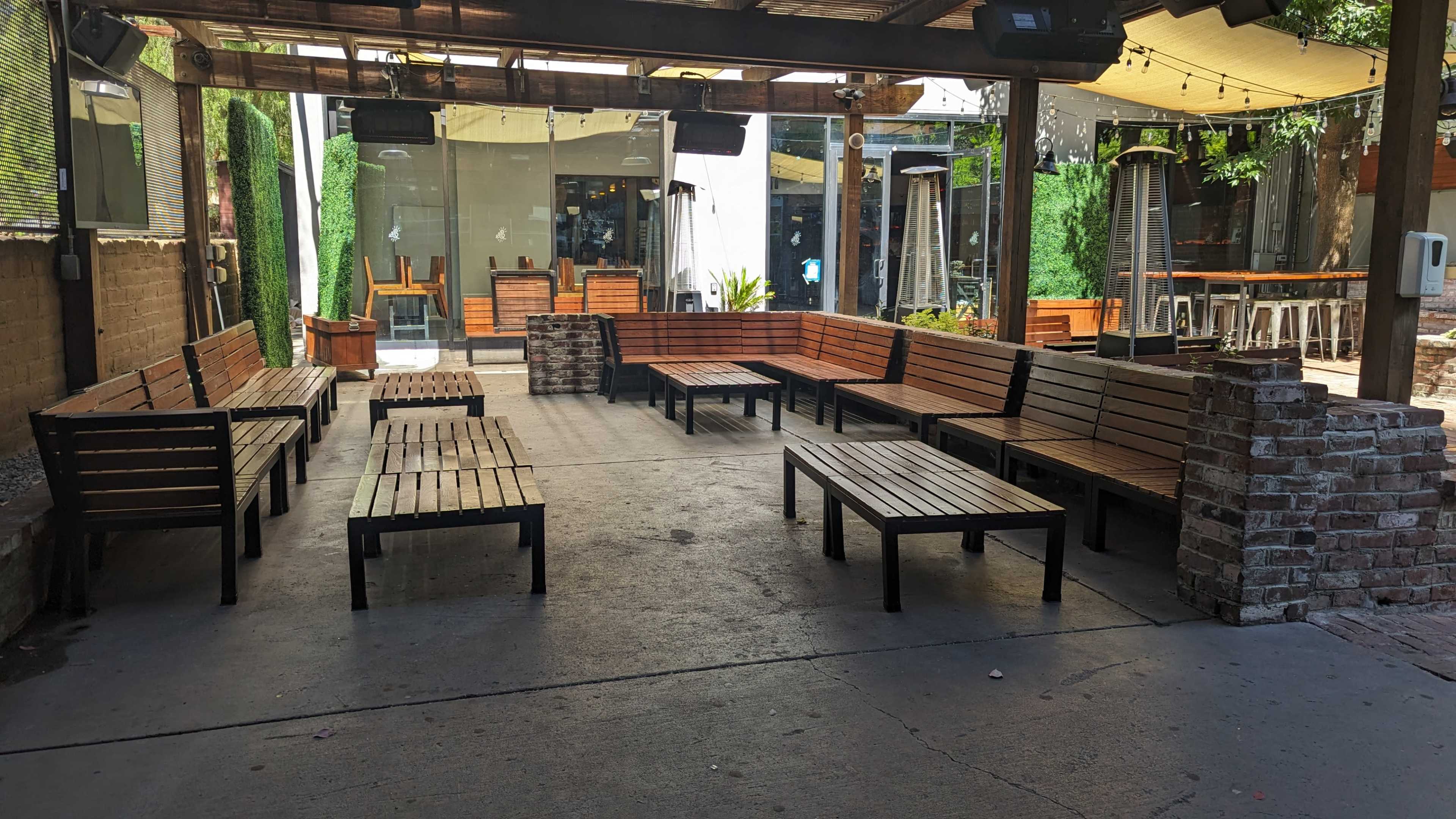 The image shows a spacious outdoor seating area with wooden benches and tables arranged around a central open space.
