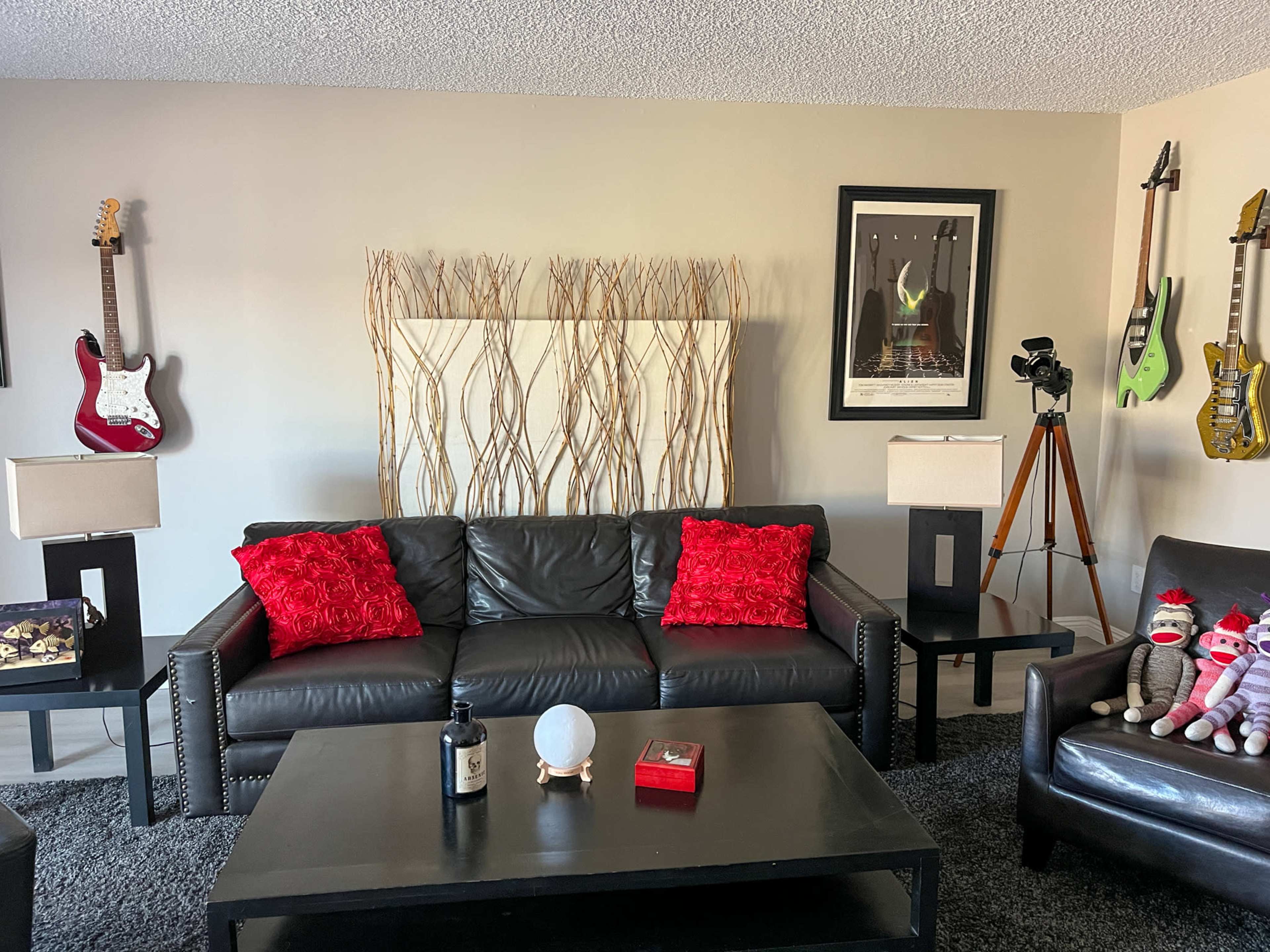 The living room features a black leather sofa with red pillows, accompanied by a black coffee table, decorative wall art, and guitars mounted on the walls.
