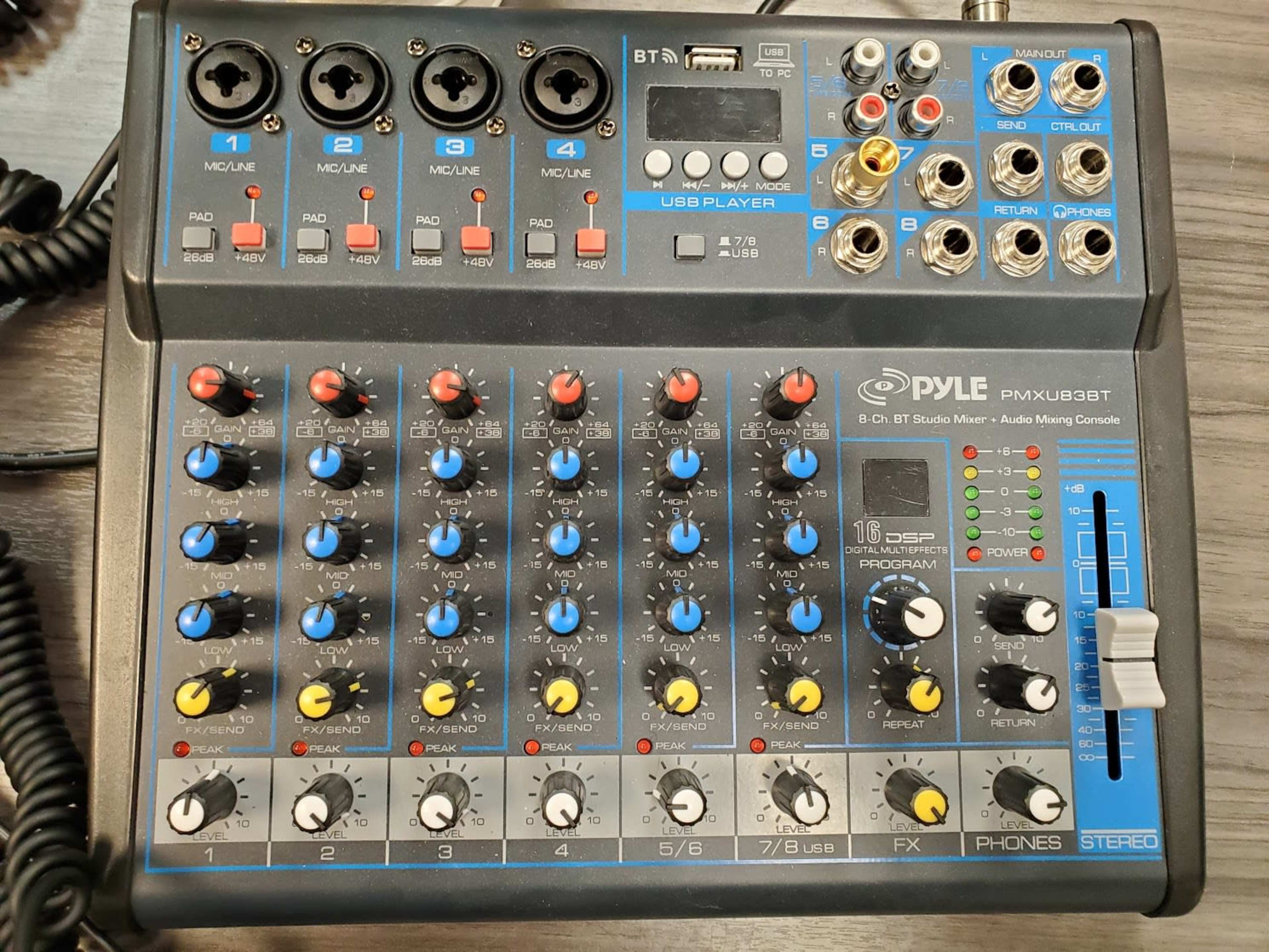 A Pyle PMXUBT professional audio mixing console with multiple channels, knobs, and input ports on a wooden surface.