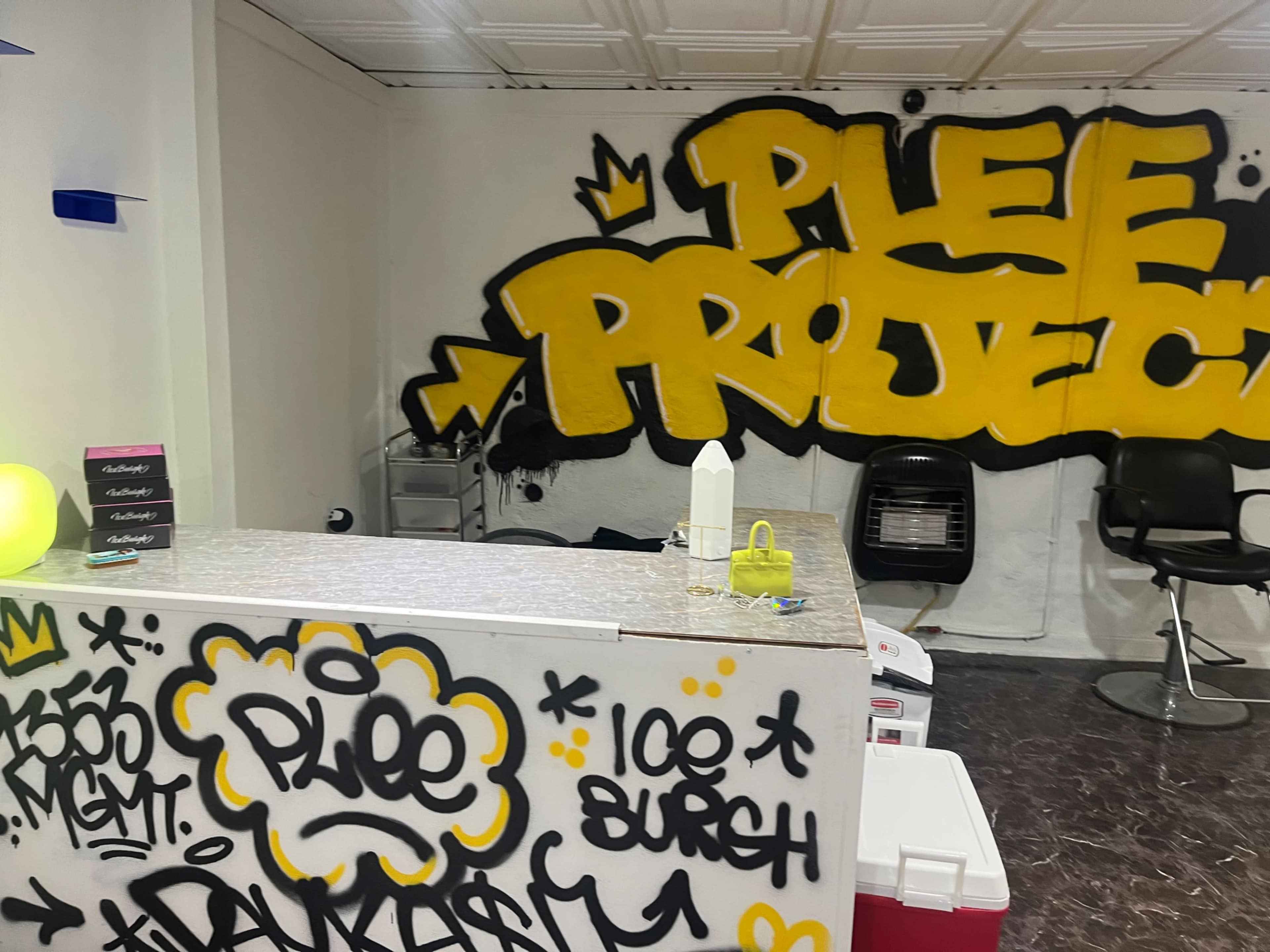 An interior space featuring a reception area with a countertop, barbershop chairs, and vibrant graffiti on the walls.