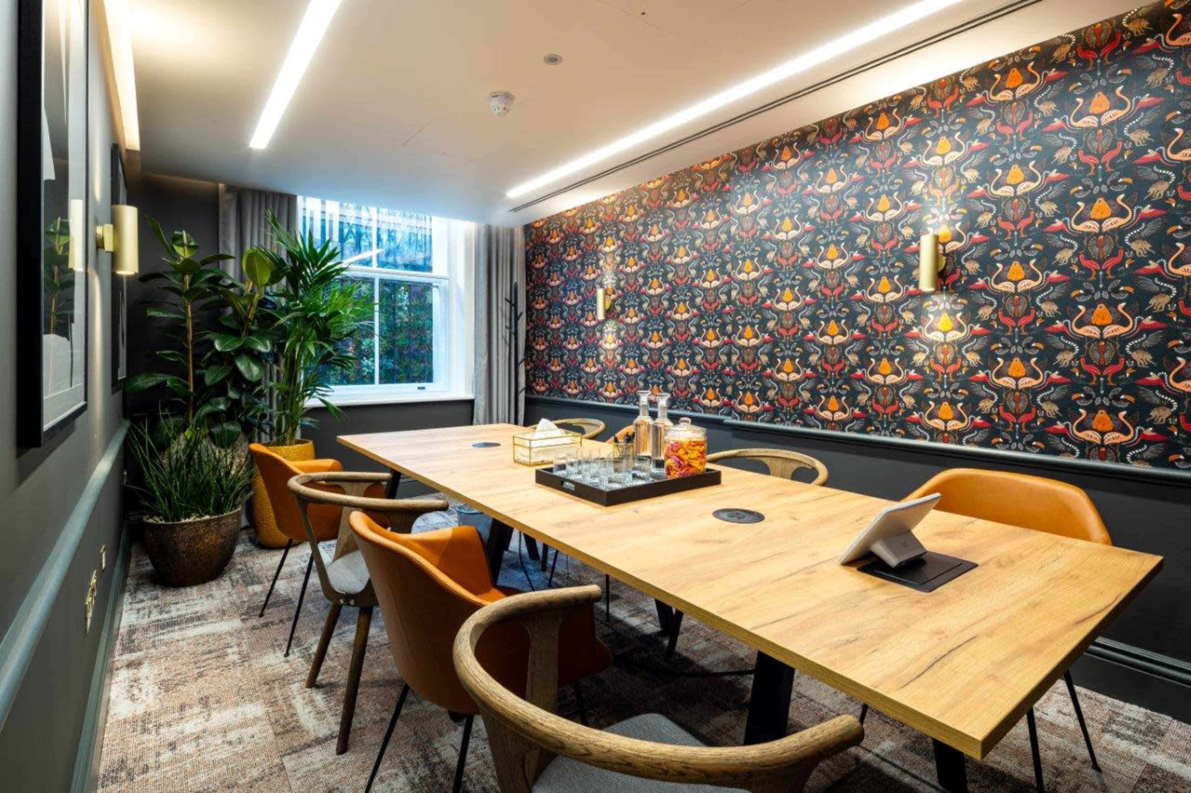 A modern conference room features a large wooden table surrounded by chairs, a patterned accent wall, and decorative plants.