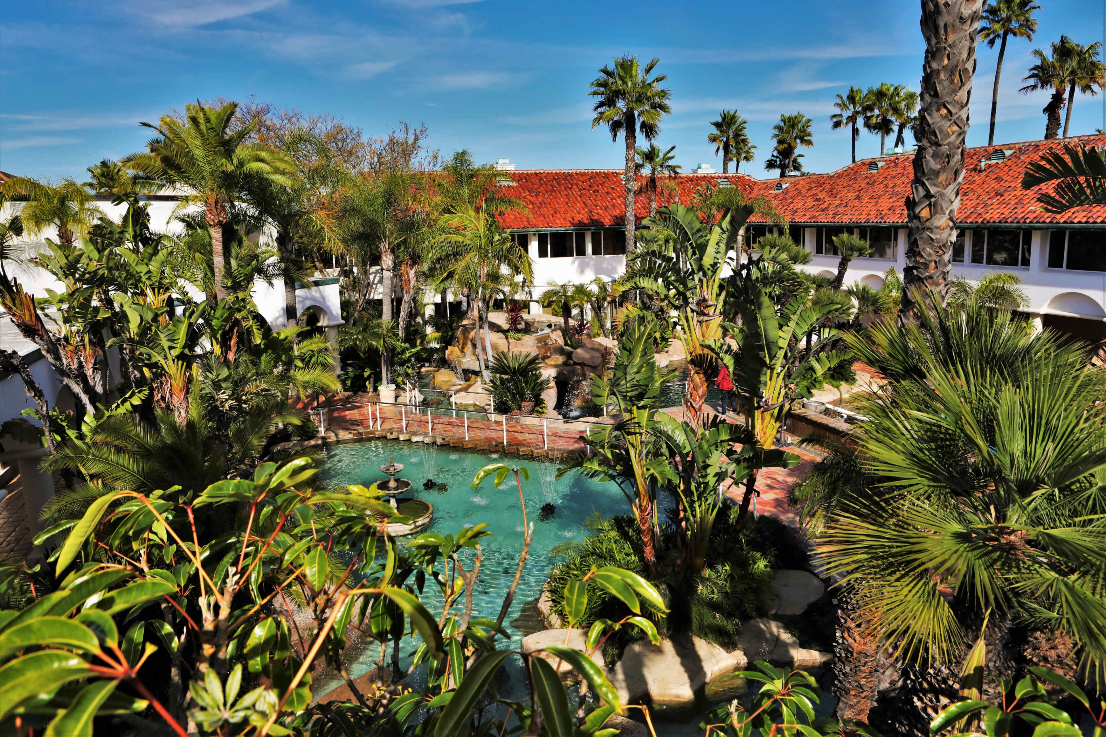 A tropical resort courtyard featuring a pool surrounded by palm trees and landscaped gardens.