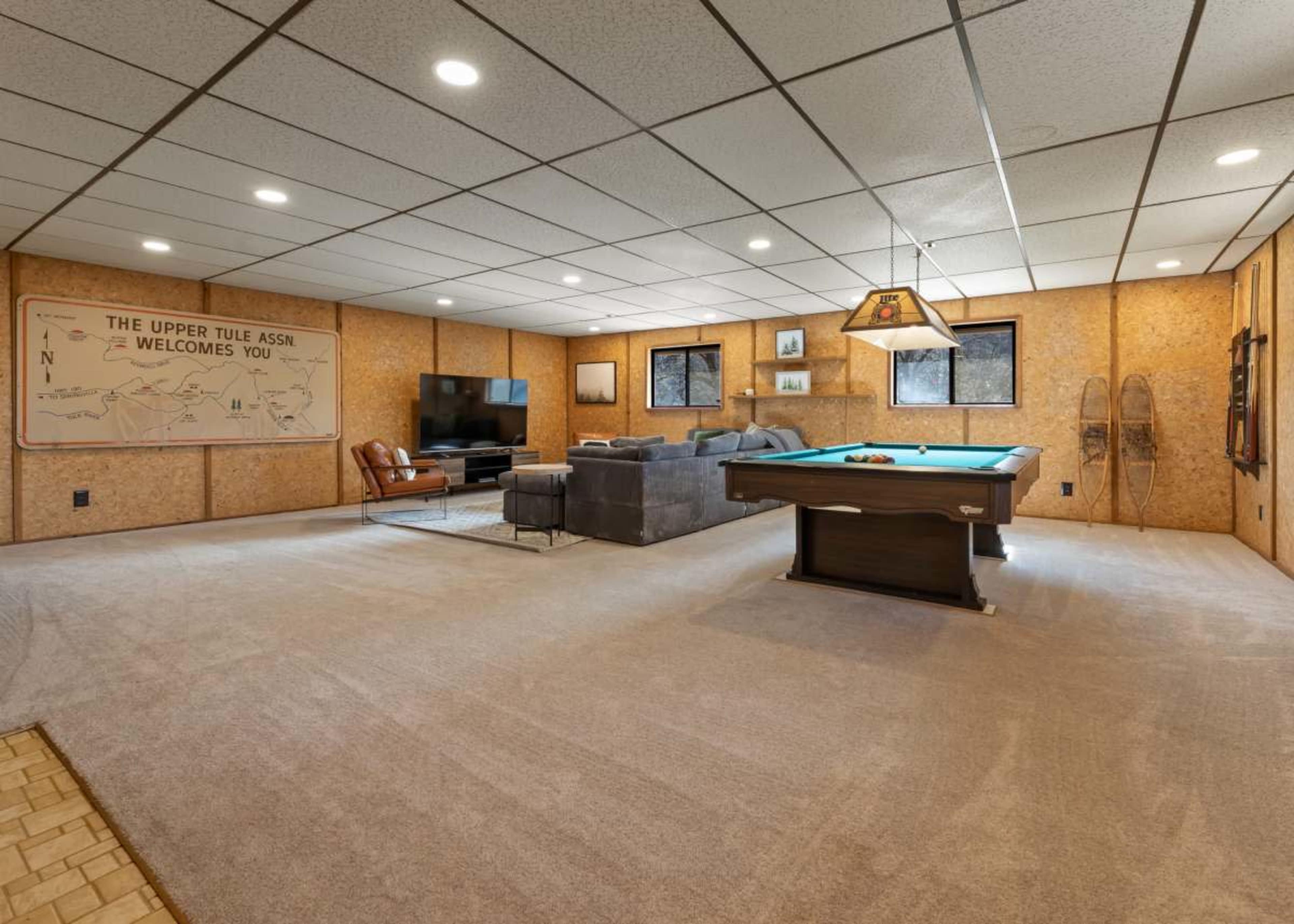 A spacious basement recreation room featuring a pool table, a sectional sofa, and wall-mounted decorations.