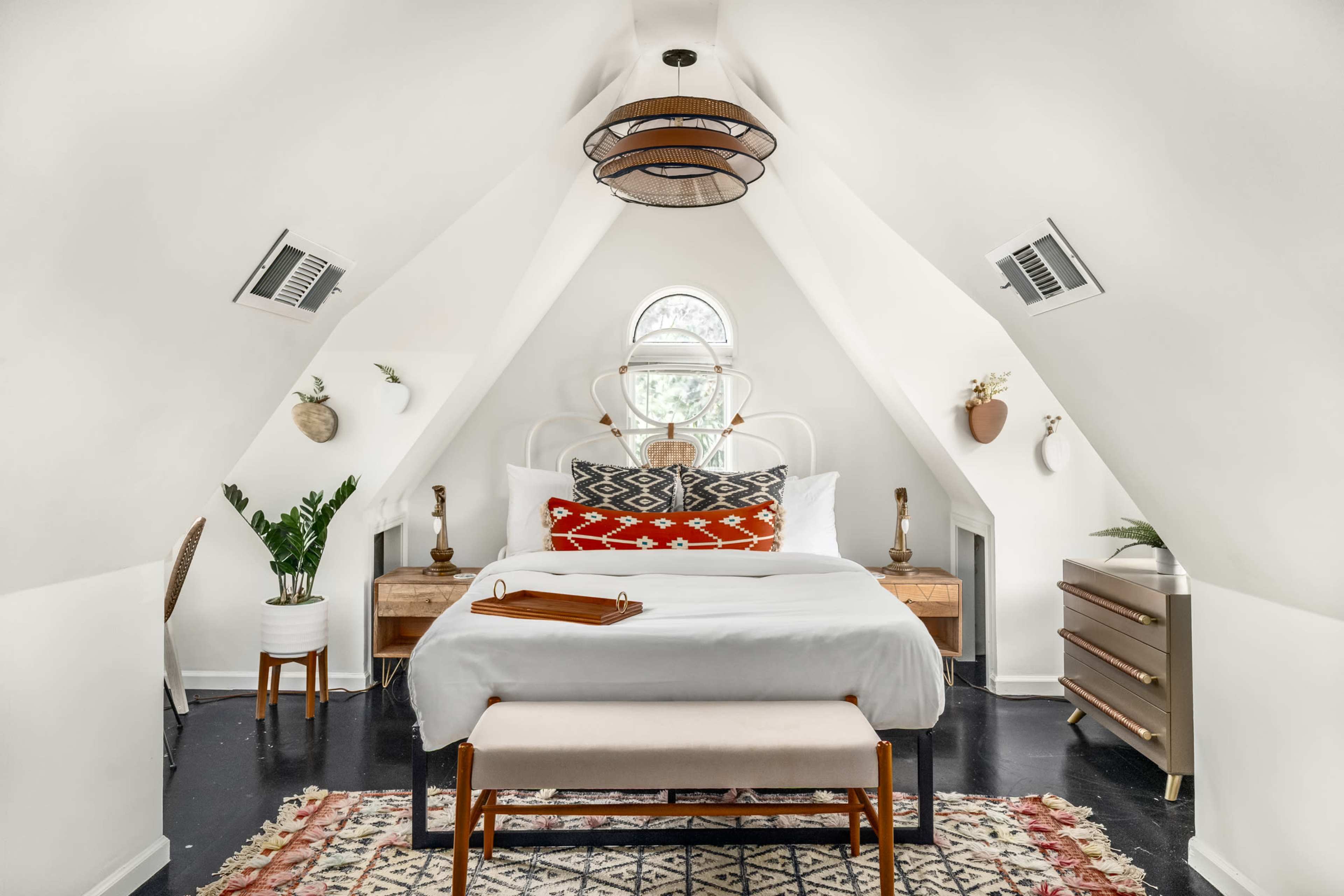 A cozy bedroom features a bed with white linens, an ornate ceiling, and decorative plants and furnishings.