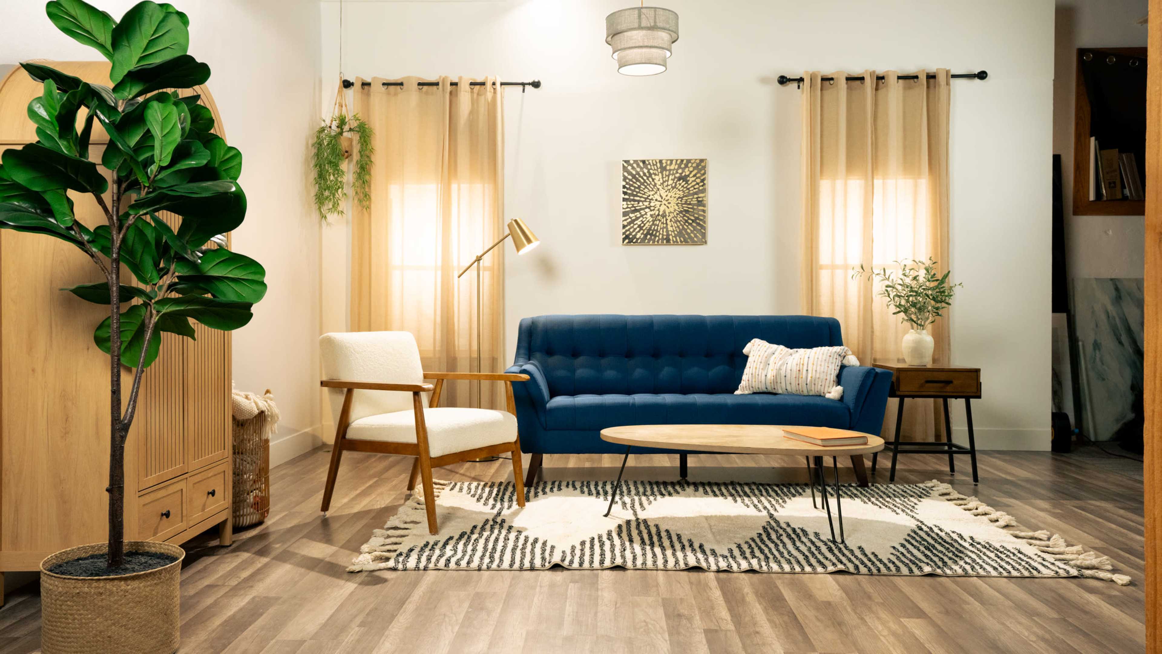 A modern living room features a blue couch, a white armchair, a round coffee table, and decorative elements like a plant and patterned rug.
