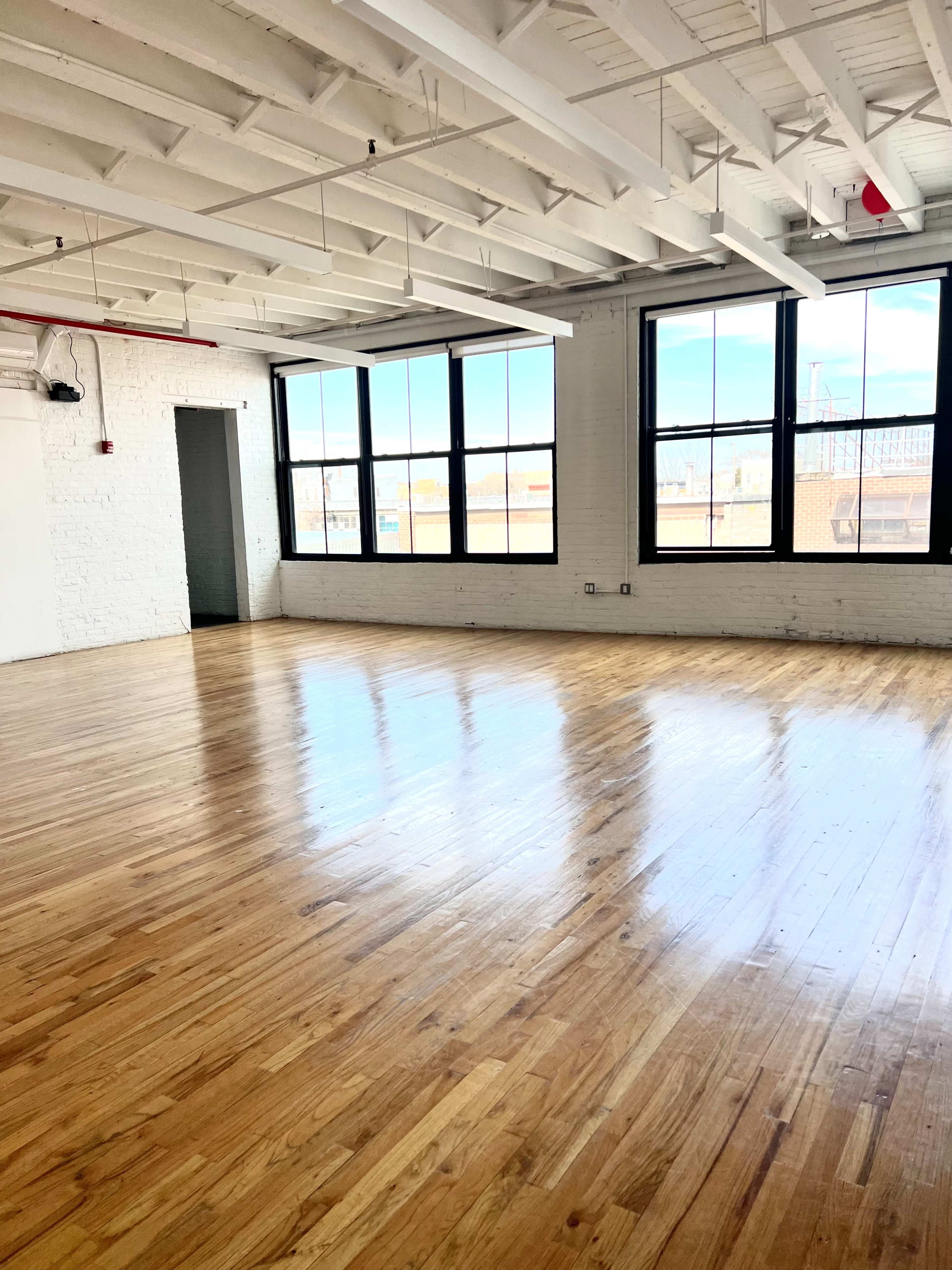 A spacious, light-filled room with hardwood floors and large windows.