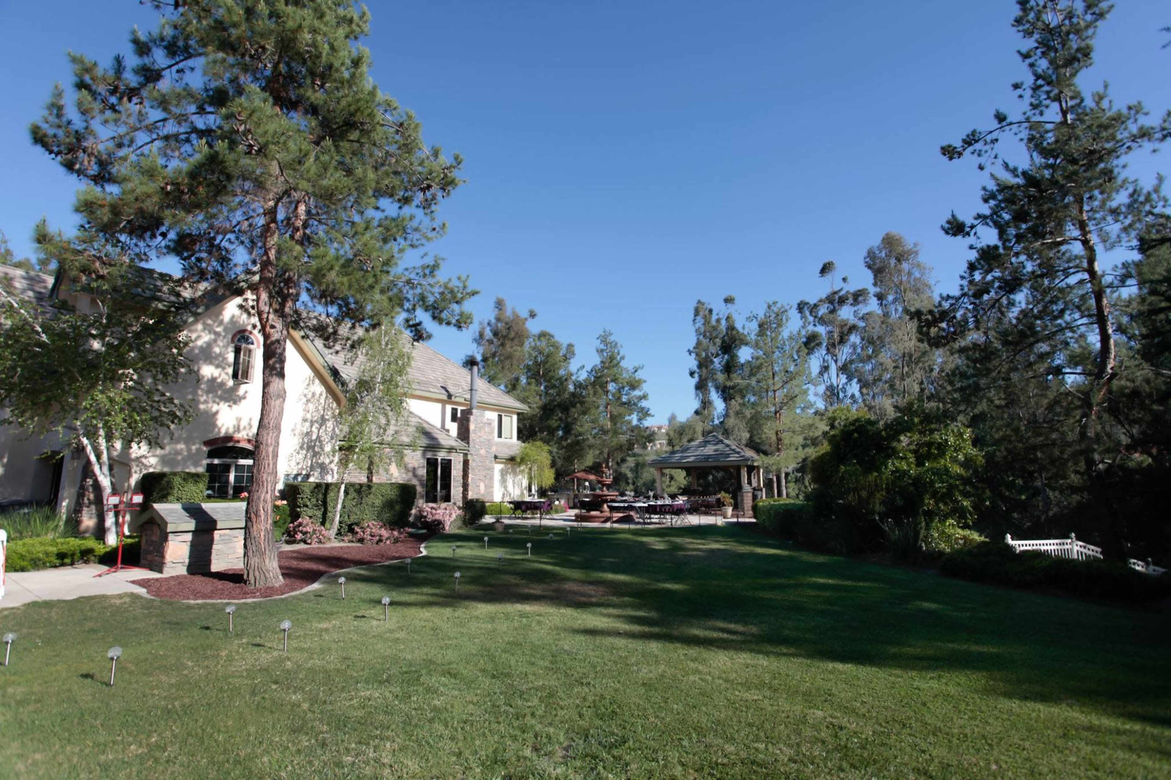 A spacious backyard features a two-story house, a gazebo, and well-maintained landscaping under clear blue skies.