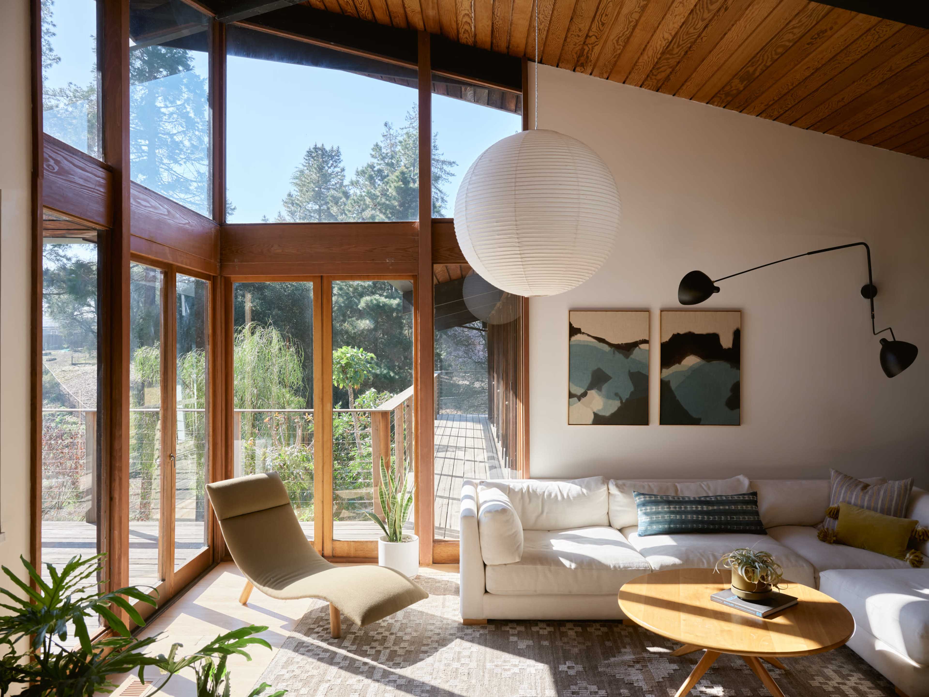 The image shows a bright living room with large windows, a white sofa, a wooden coffee table, and modern decor elements.