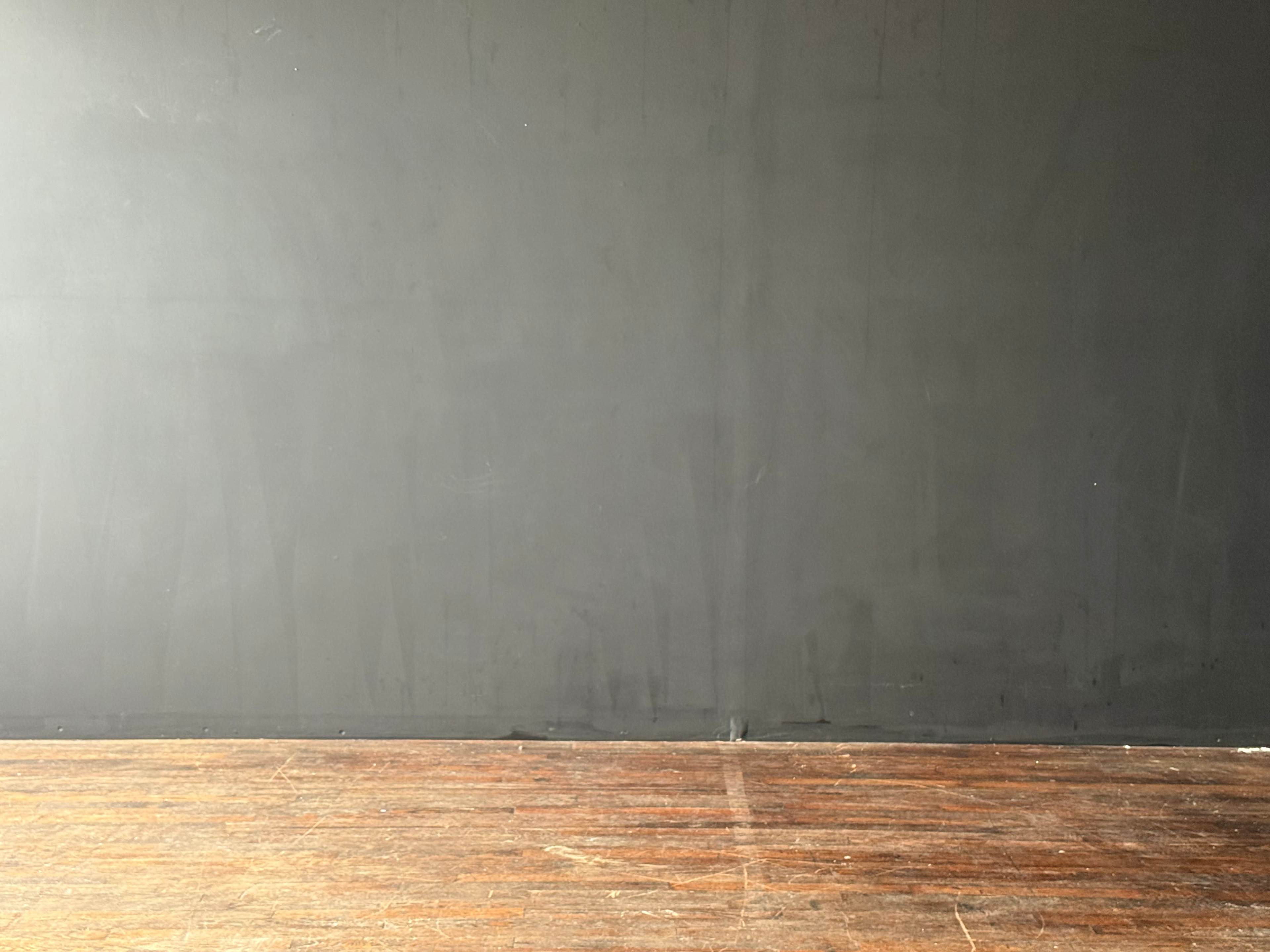 A simple room features a dark gray wall and a wooden floor.