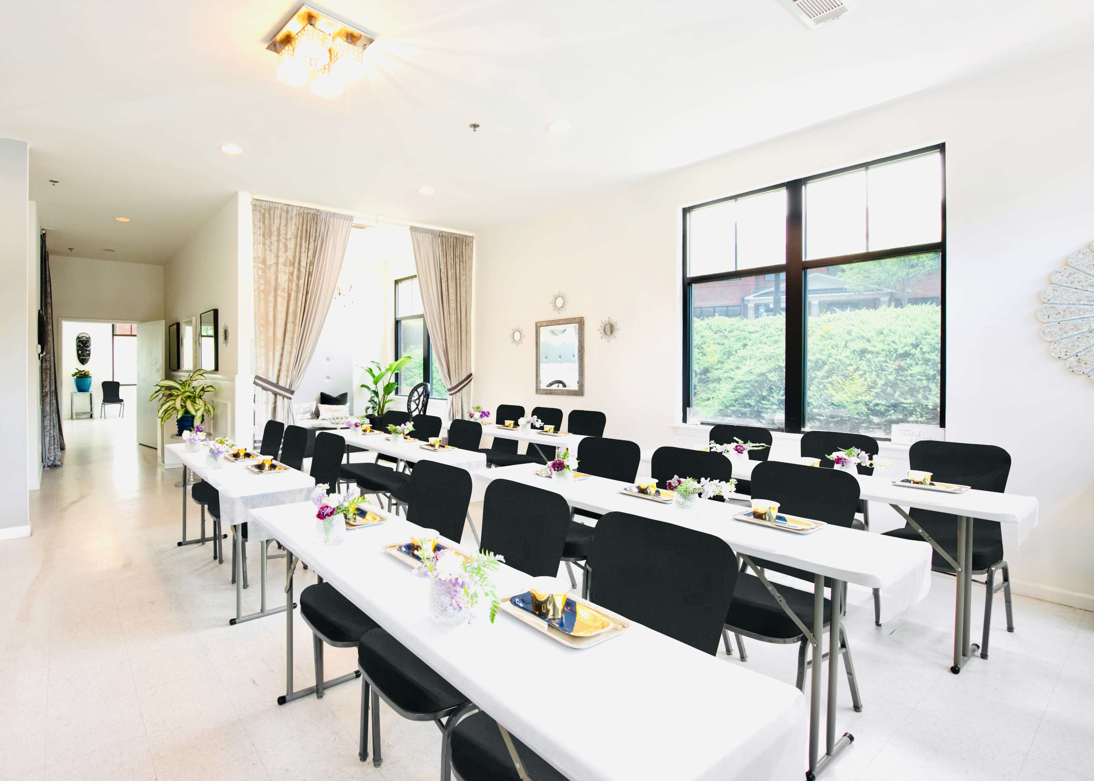 A set up for a dining event with rows of tables adorned with plates and floral centerpieces in a bright, modern room.