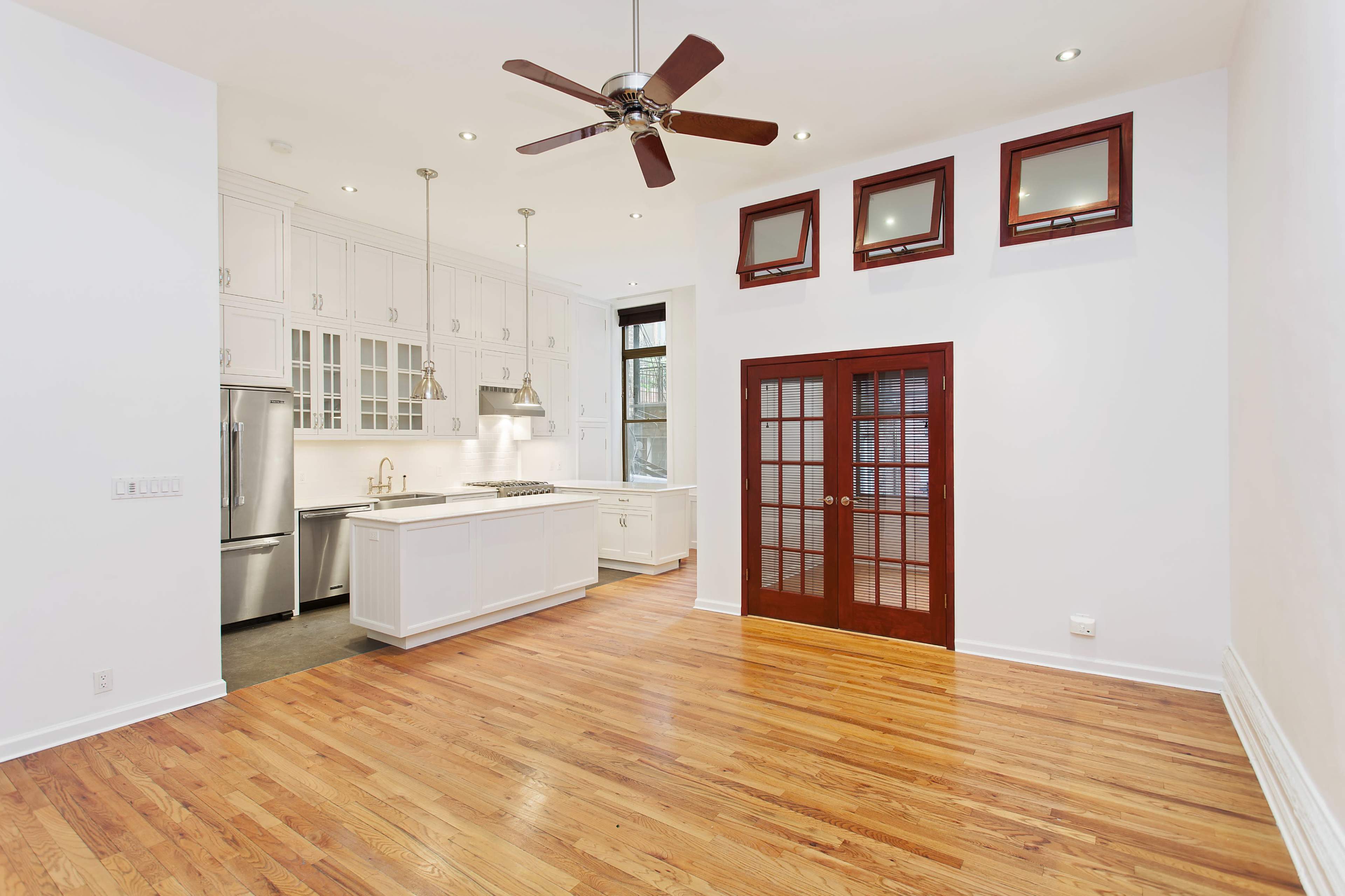 A modern kitchen and living area with hardwood floors, white cabinetry, and a set of double doors leading to another room.
