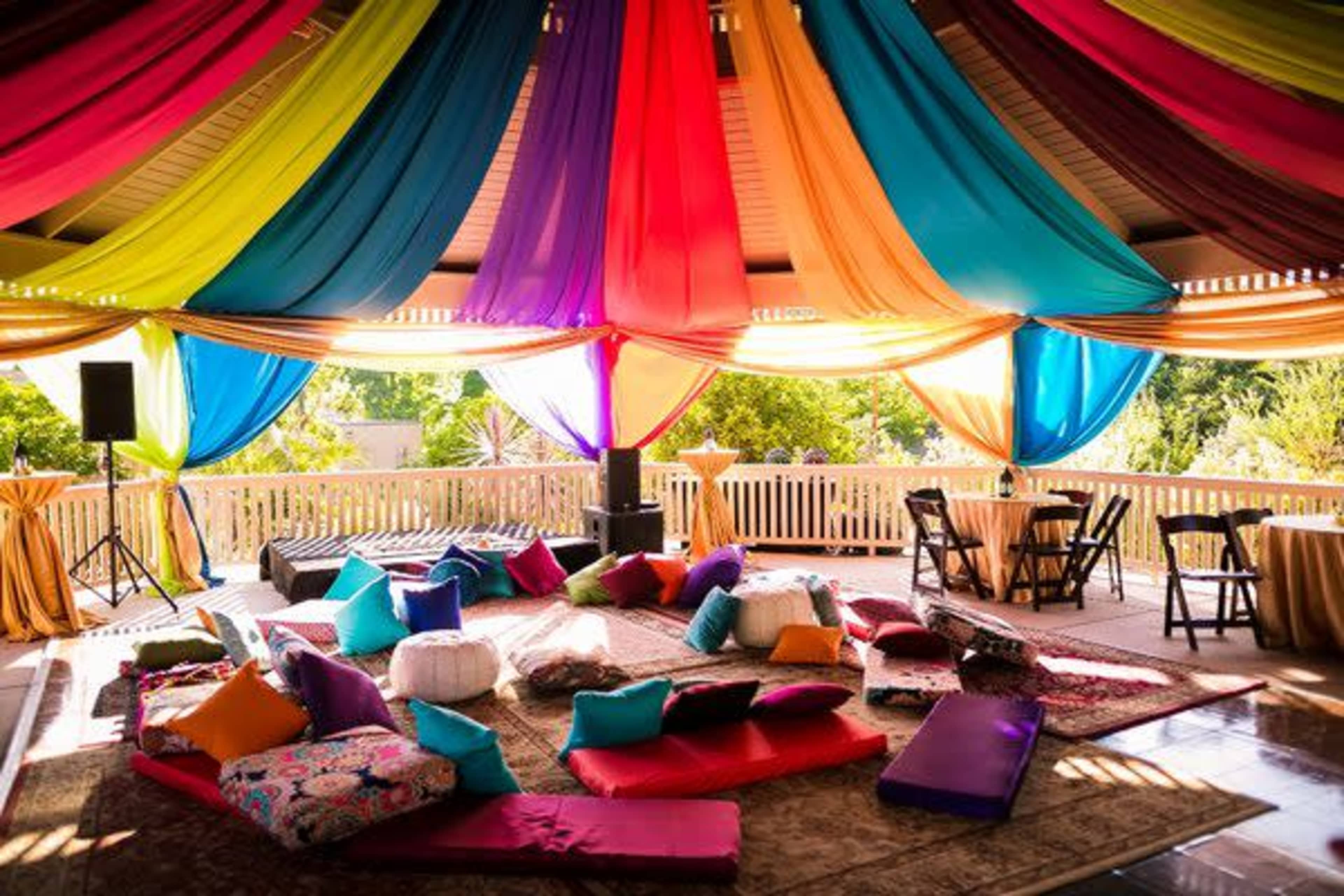 A vibrant indoor space with colorful drapes hanging from the ceiling, accented by cushions and low seating arranged on a patterned rug.